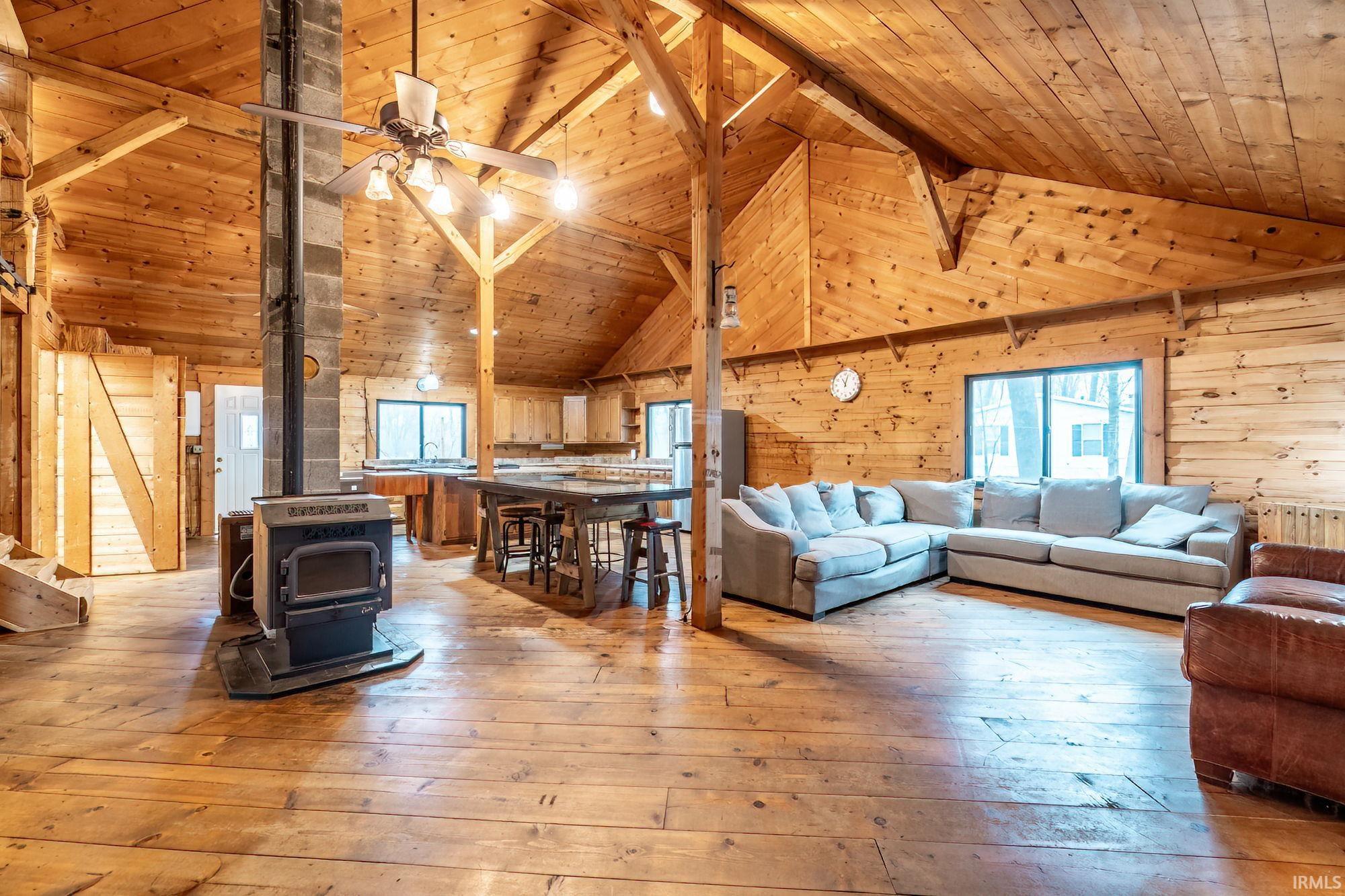 Living room featuring a high wood beamed ceiling, light wood-type flooring, a ceiling fan, a wood stove, and wood walls