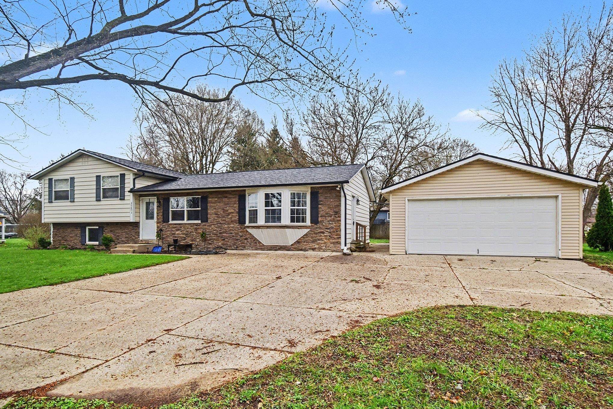 Split level home featuring a garage, an outdoor structure, brick siding, and a front lawn