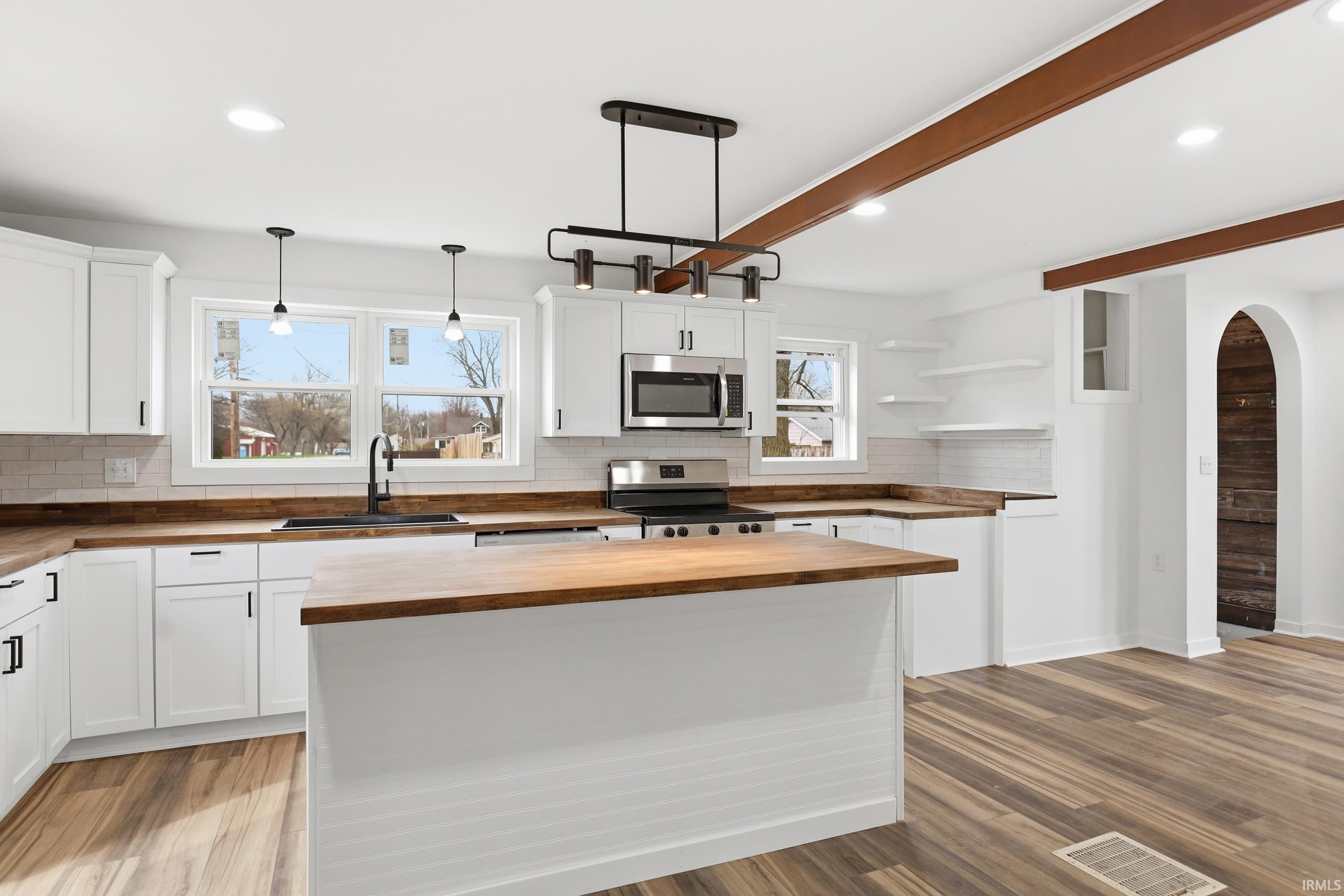 Kitchen with wooden counters, arched walkways, backsplash, stainless steel appliances, and light wood-type flooring
