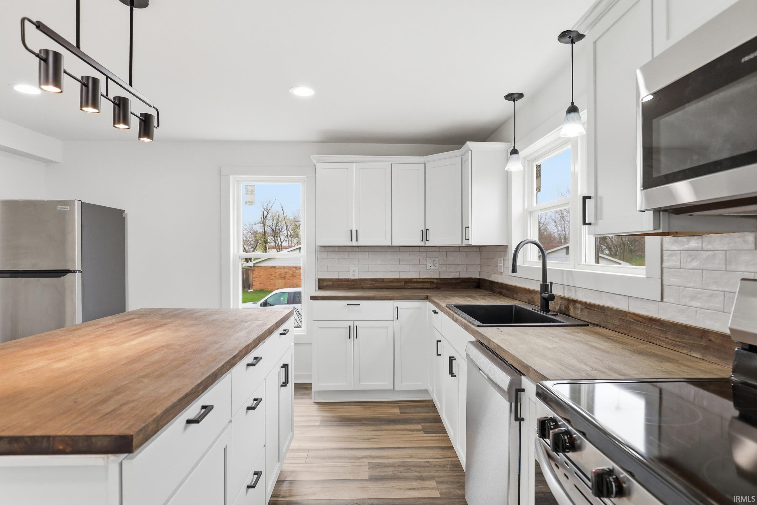 Kitchen with butcher block countertops, stainless steel appliances, white cabinets, pendant lighting, and decorative backsplash