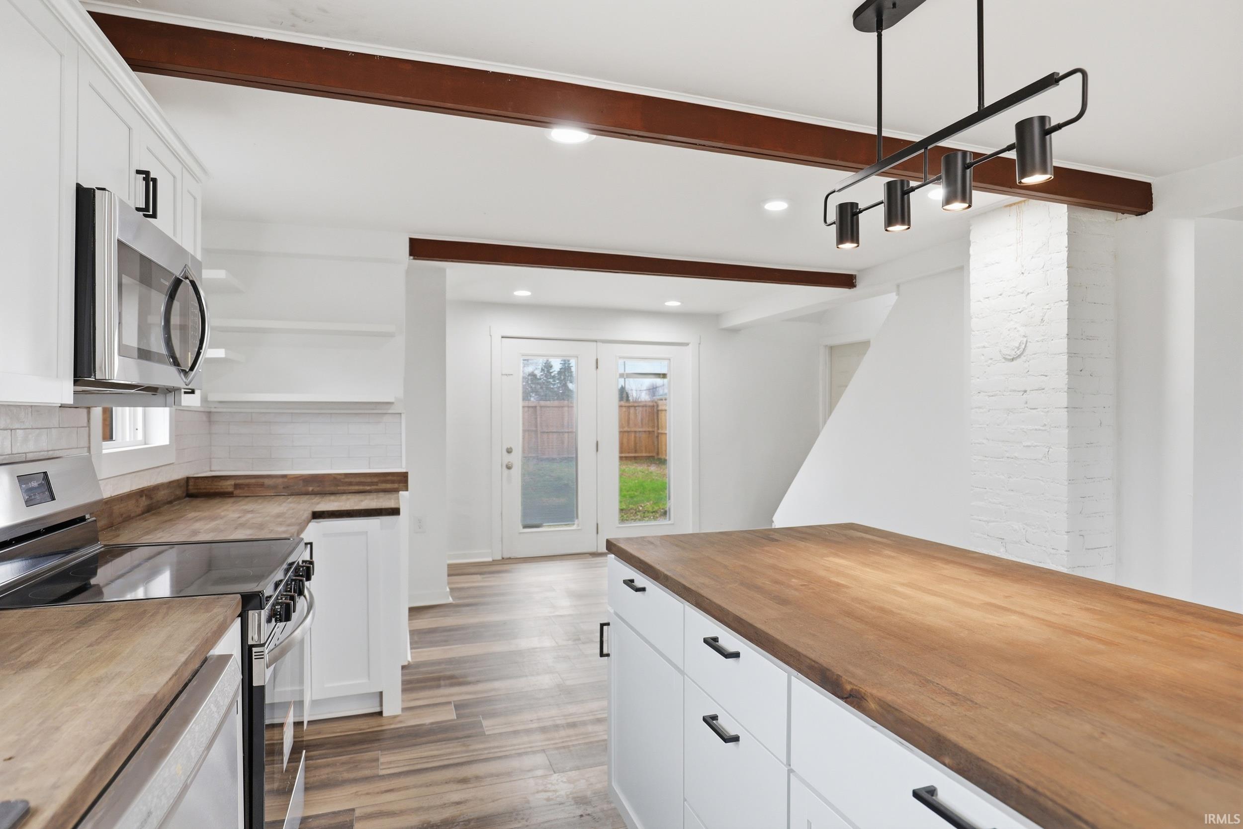 Kitchen with butcher block countertops, stainless steel appliances, white cabinets, open shelves, and beam ceiling