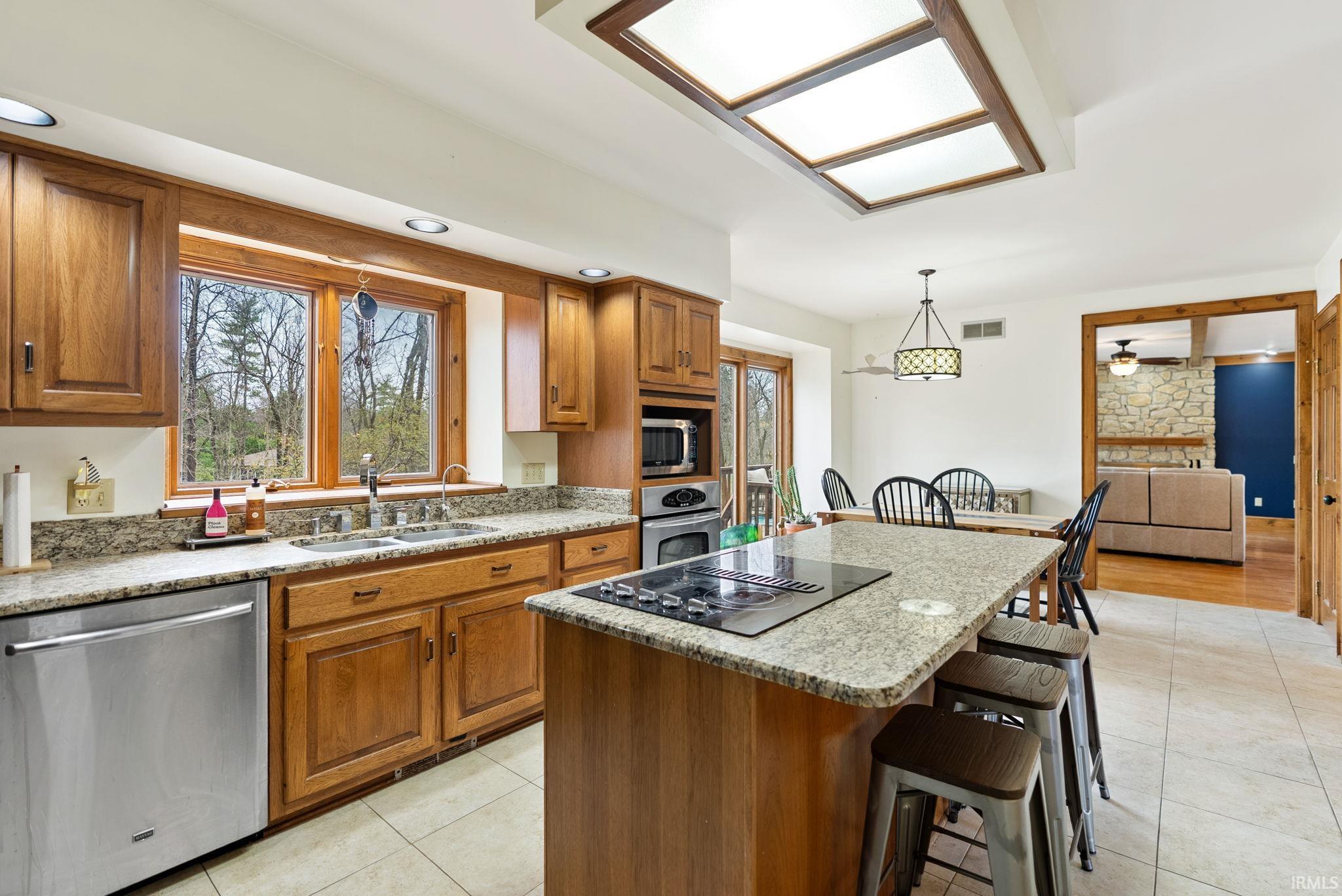 Kitchen with wood finish cabinets, stainless steel appliances, light stone countertops, and a kitchen breakfast bar