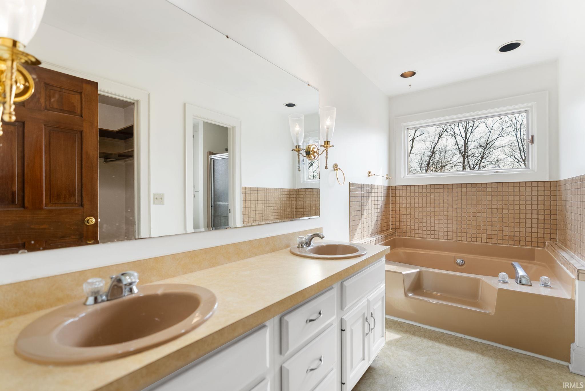 Bathroom featuring double vanity, a bath, a stall shower, and light flooring