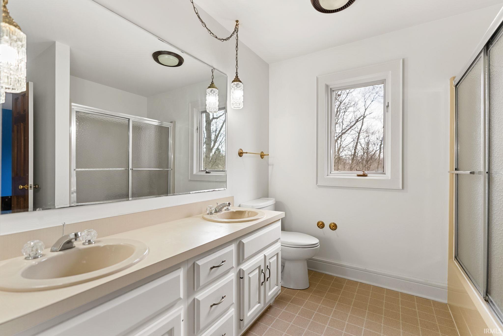 Full bath with double vanity, light tile patterned floors, and bath / shower combo with glass door