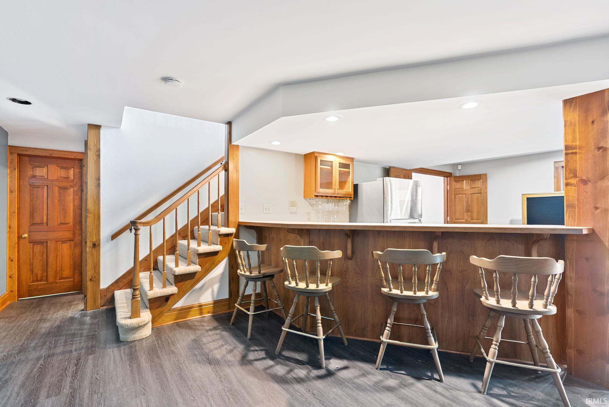 Indoor dry bar featuring glass insert cabinets, freestanding refrigerator, recessed lighting, wood finish cabinetry, and dark wood-style flooring