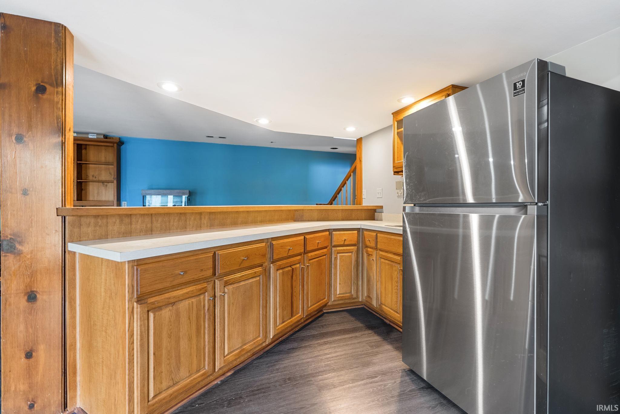 Kitchen with freestanding refrigerator, light countertops, a peninsula, wood finish cabinetry, and recessed lighting