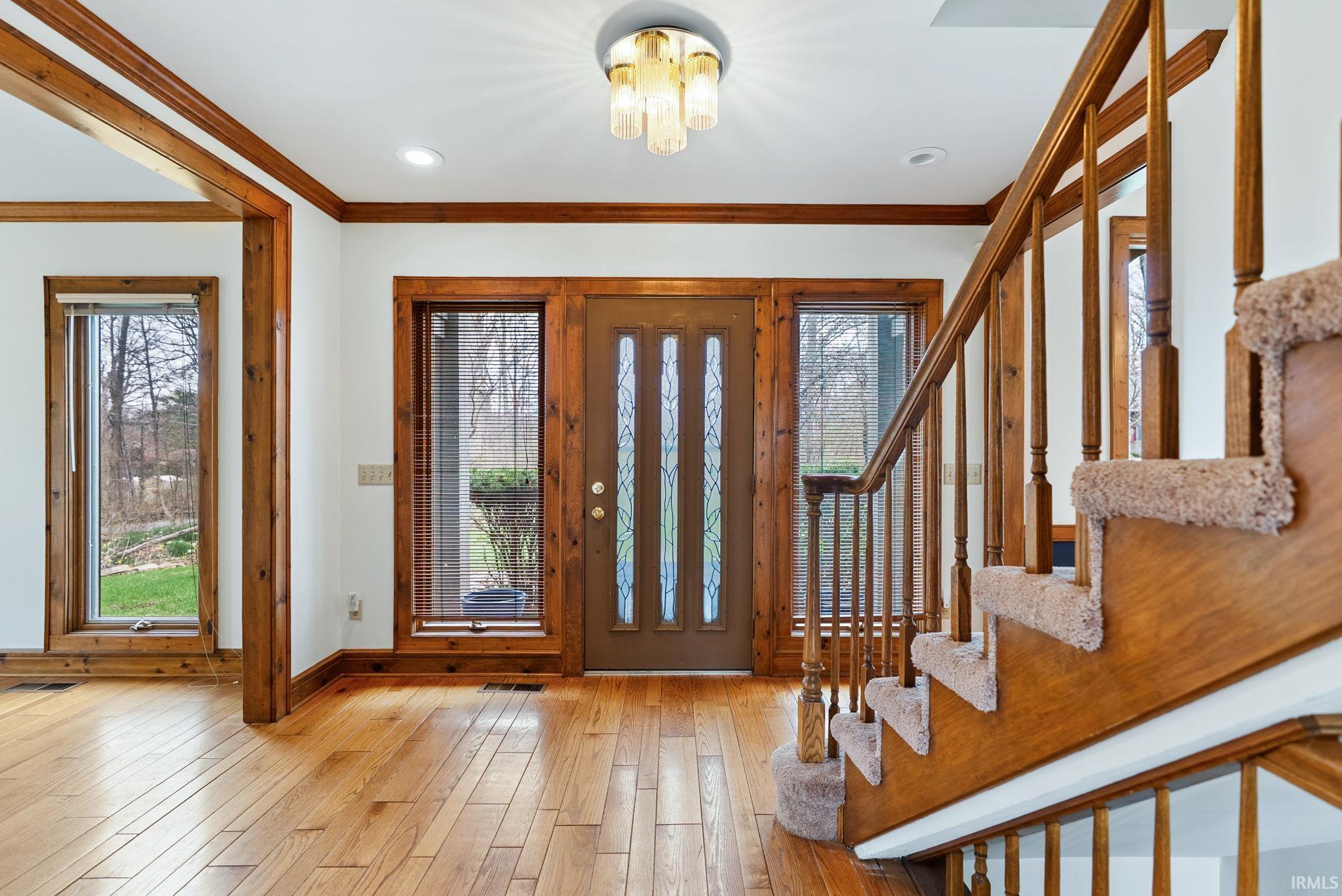 Foyer entrance with light wood finished floors, crown molding, plenty of natural light, and a chandelier