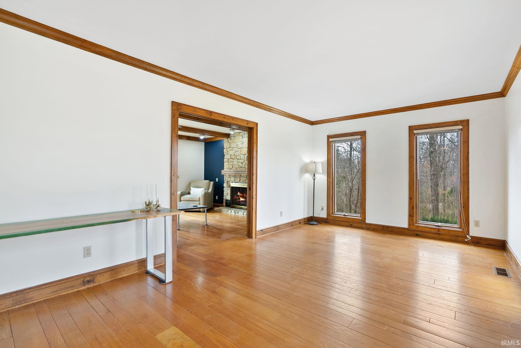 Empty room featuring light wood finished floors, a stone fireplace, and ornamental molding