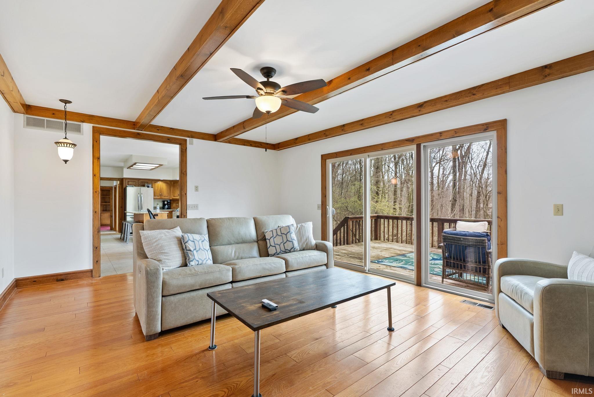 Living area featuring a ceiling fan, beamed ceiling, and light wood-type flooring