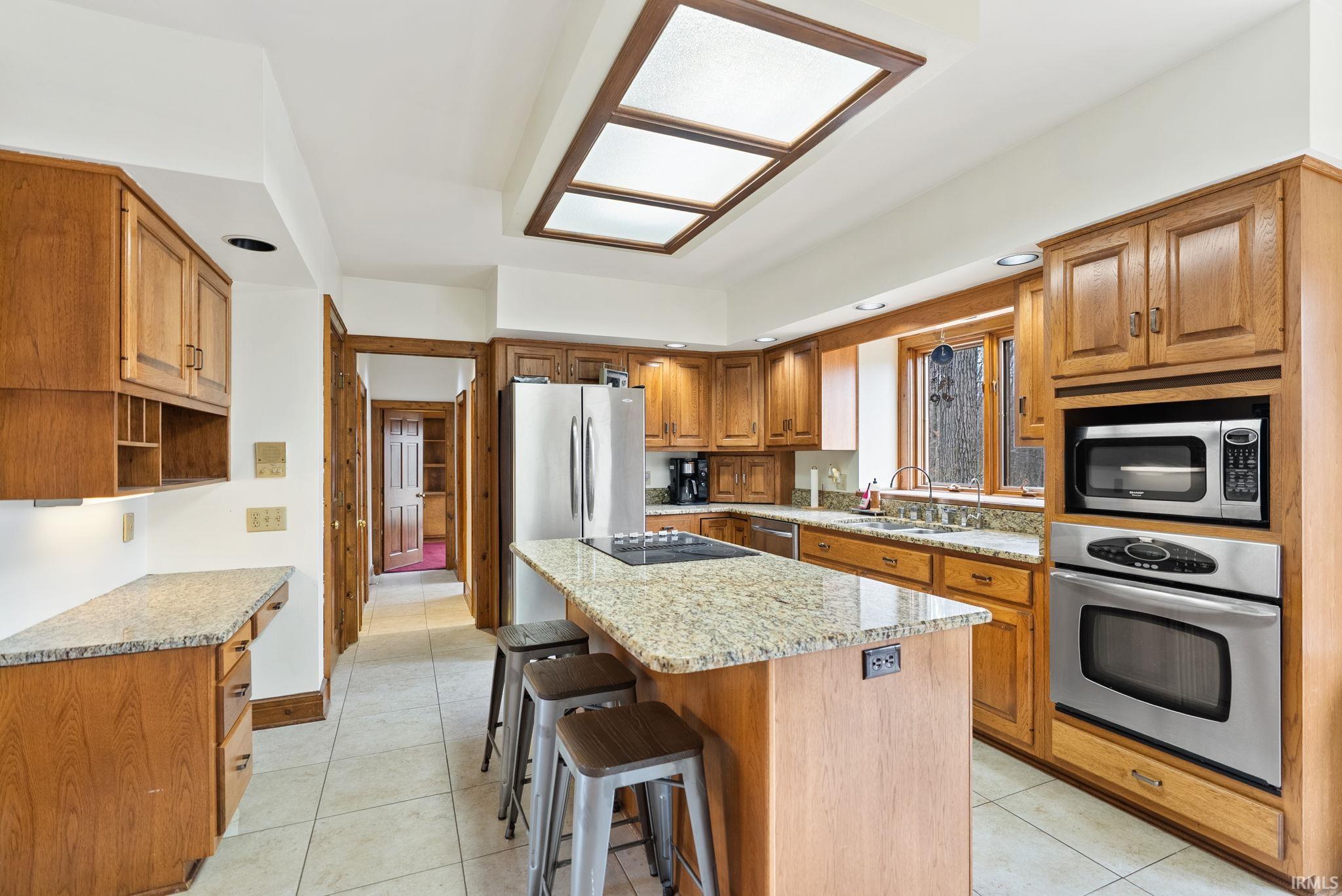 Kitchen with wood finish cabinets, stainless steel appliances, a kitchen bar, a center island, and light tile patterned floors