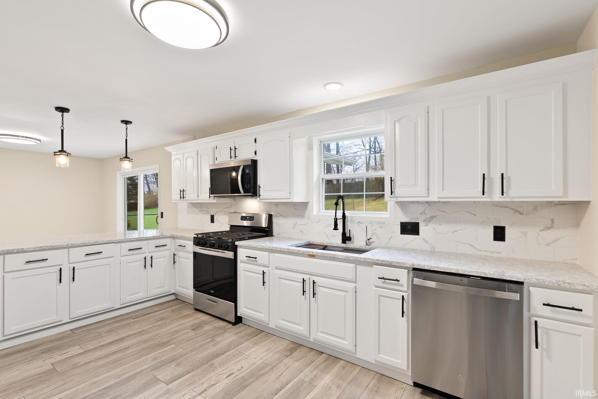 Kitchen with stainless steel appliances, white cabinetry, tasteful backsplash, and light stone counters