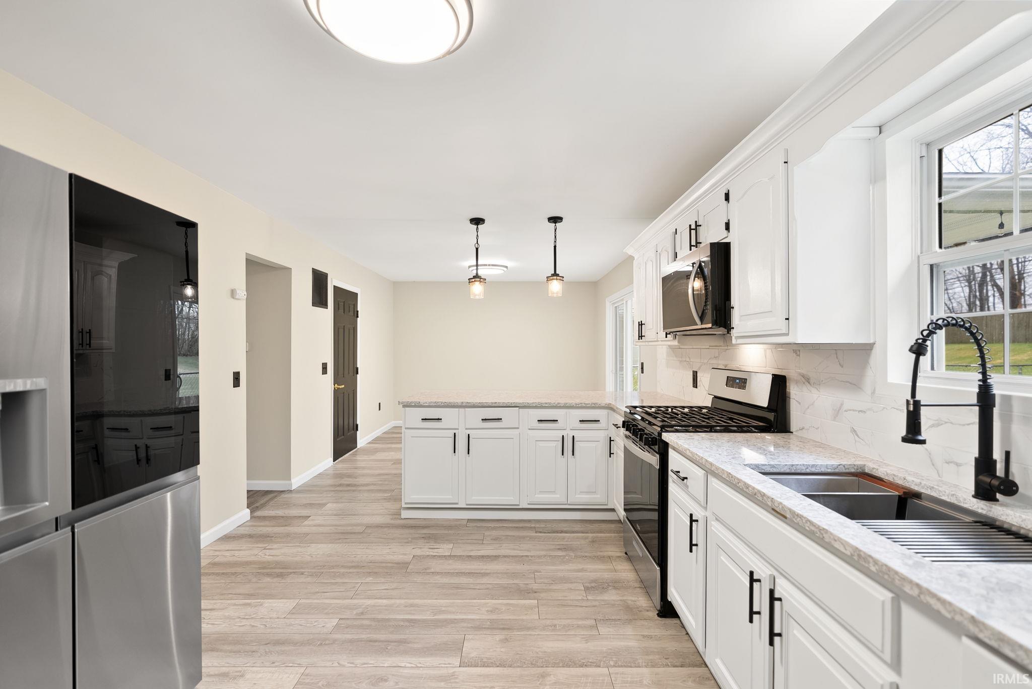 Kitchen featuring stainless steel appliances, a peninsula, tasteful backsplash, white cabinets, and light wood-style flooring