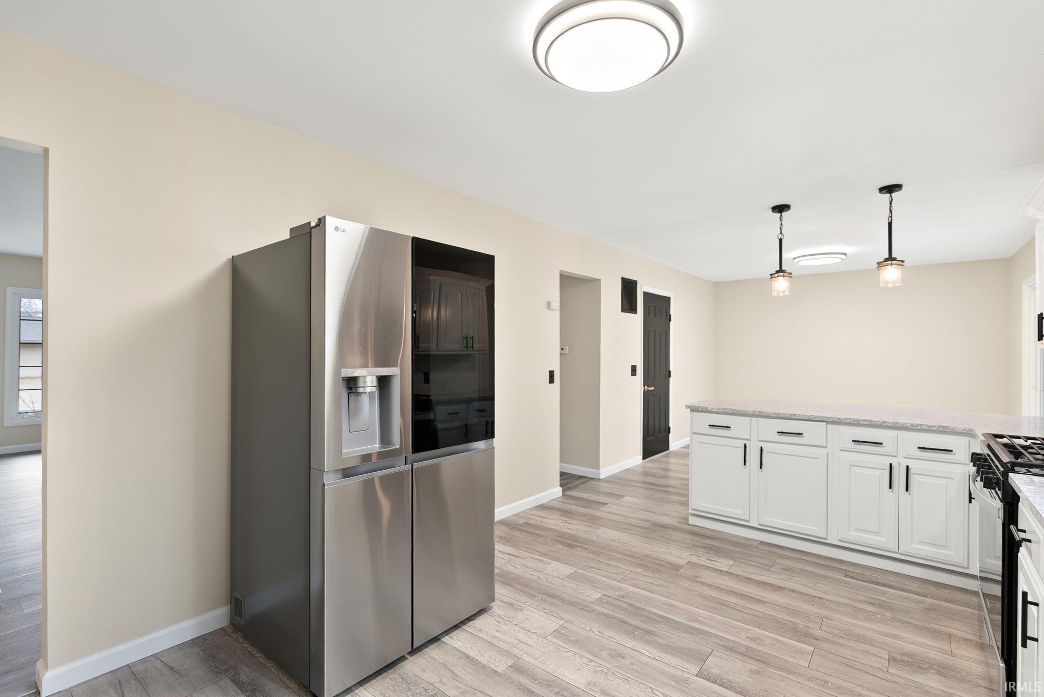 Kitchen with stainless steel fridge, light wood-style floors, hanging light fixtures, and light stone counters