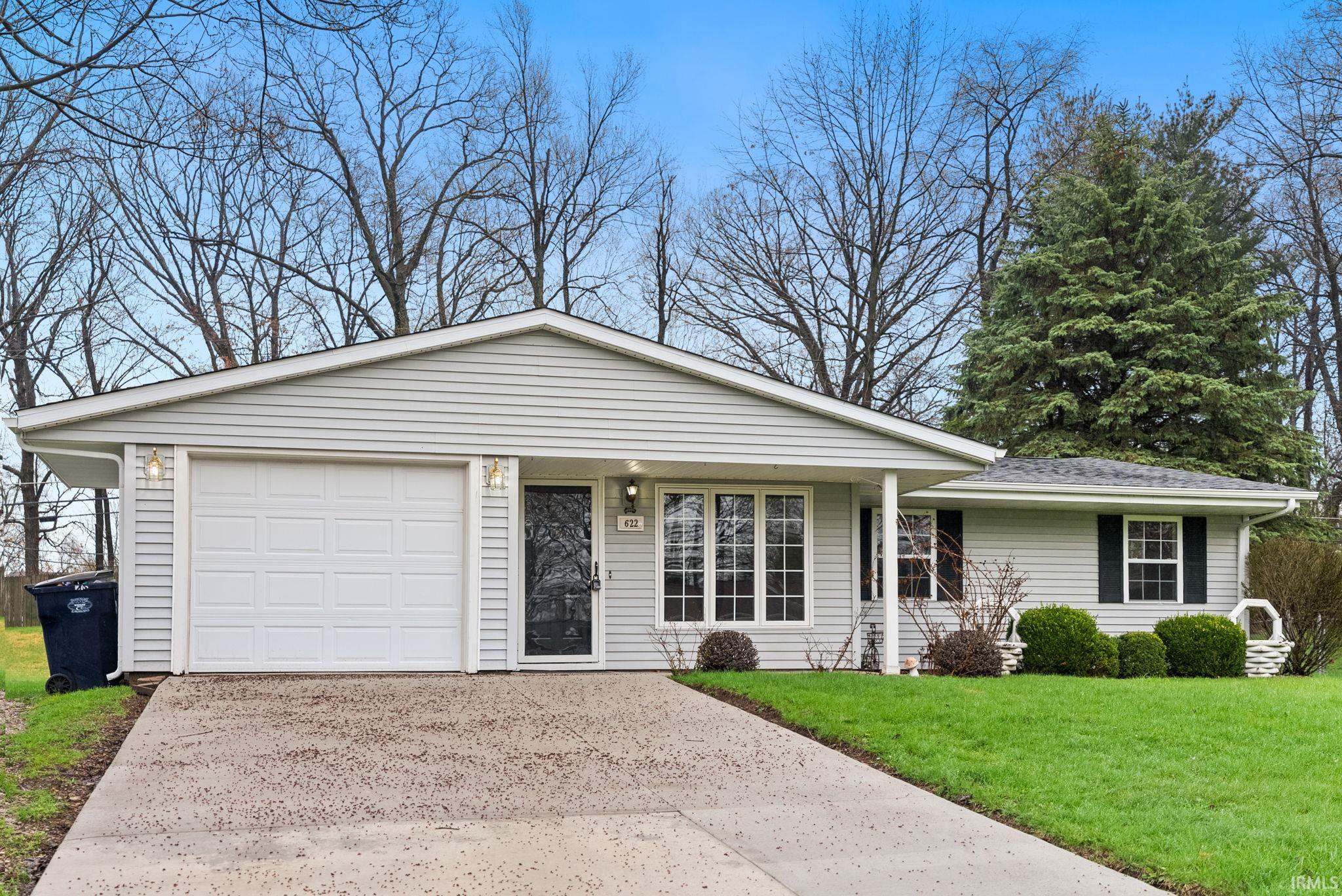 Ranch-style house featuring a front lawn, concrete driveway, an attached garage, and covered porch