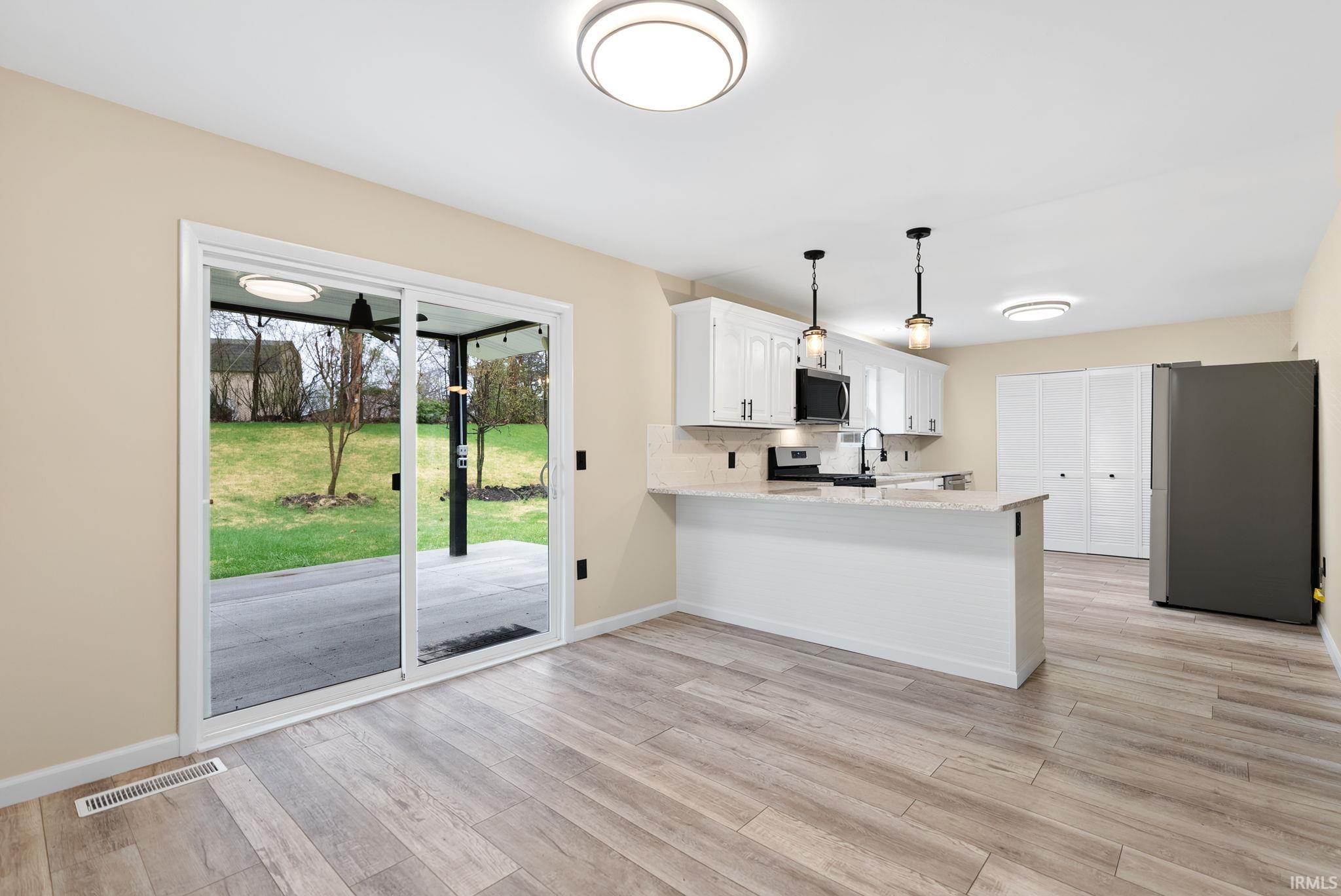 Kitchen with stainless steel appliances, white cabinetry, a peninsula, light stone counters, and light wood-style floors