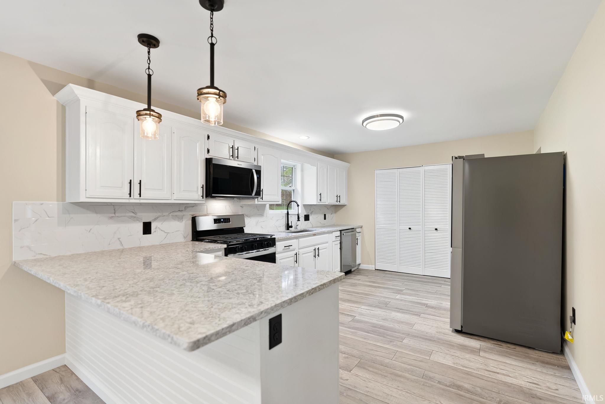 Kitchen featuring stainless steel appliances, a peninsula, white cabinets, and light wood-type flooring