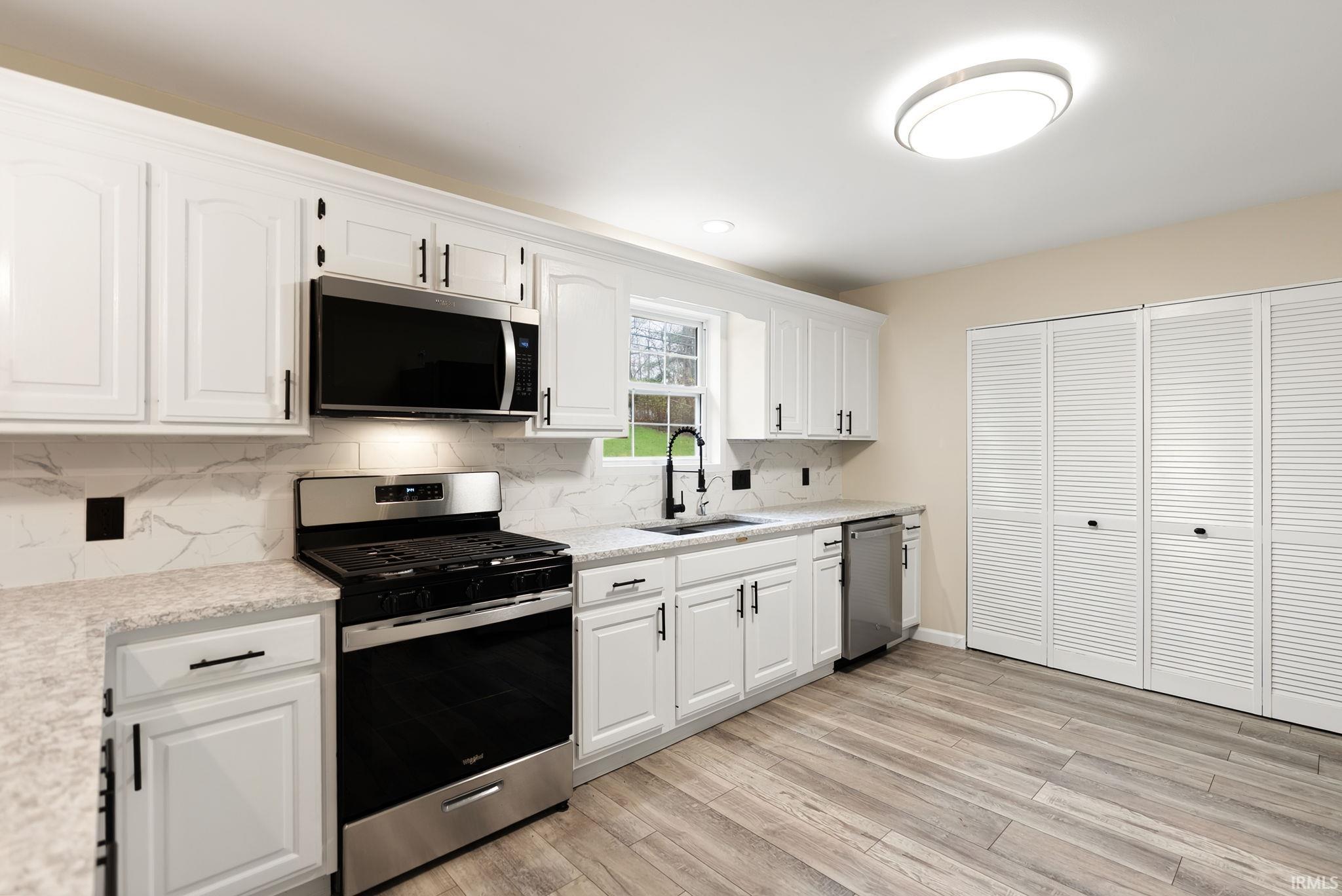 Kitchen with stainless steel appliances, white cabinets, tasteful backsplash, and light stone countertops
