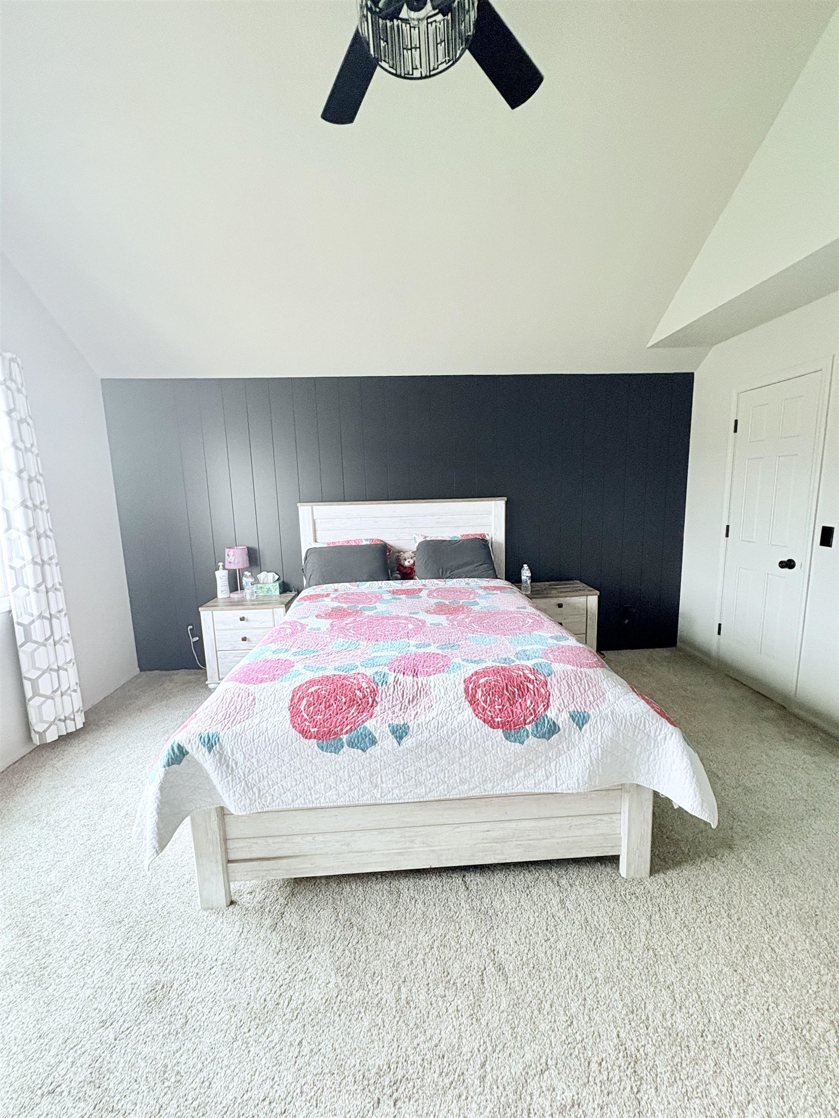 Bedroom featuring ceiling fan, light carpet, vaulted ceiling, and wooden walls