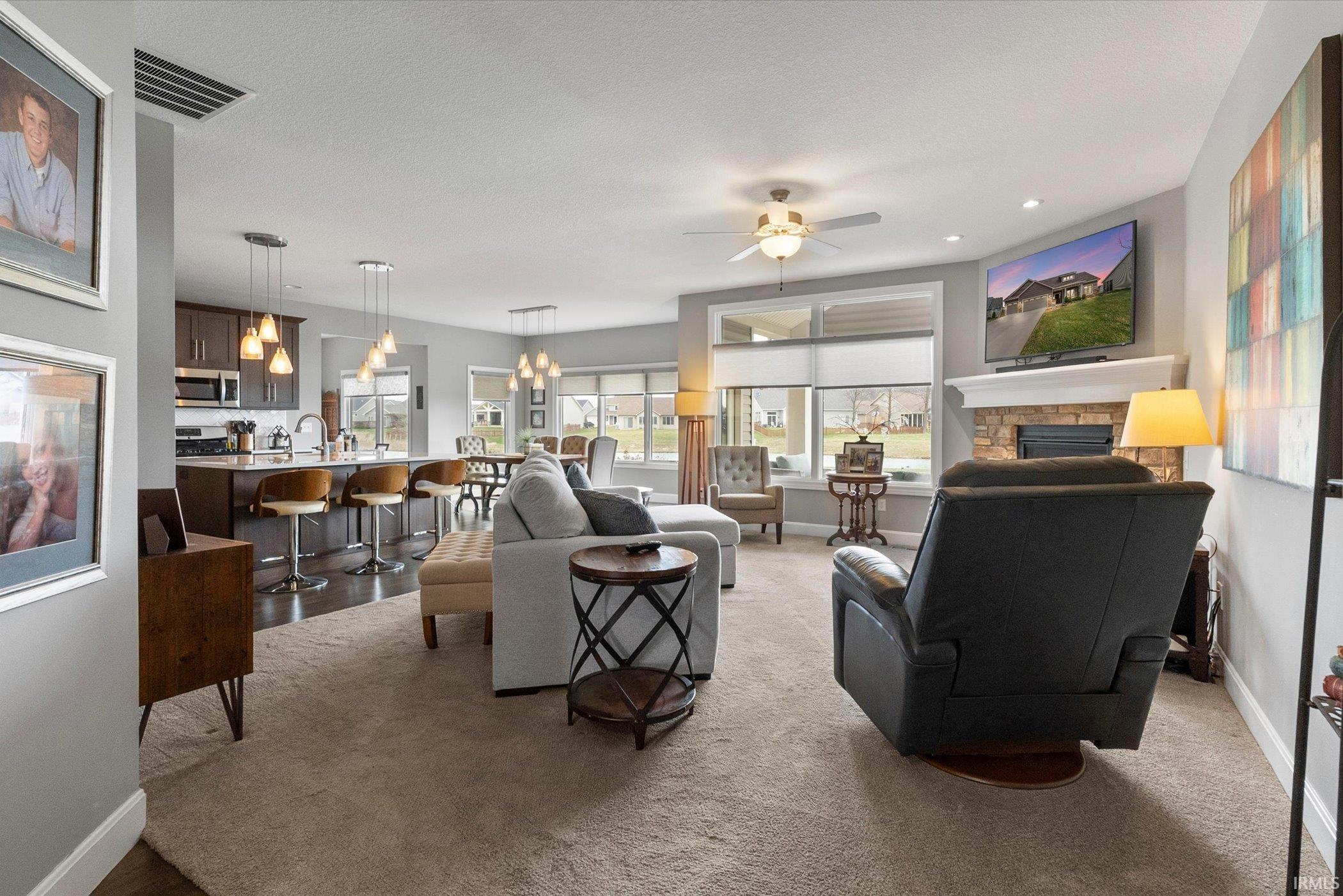 Living room featuring a stone fireplace, ceiling fan, and a chandelier