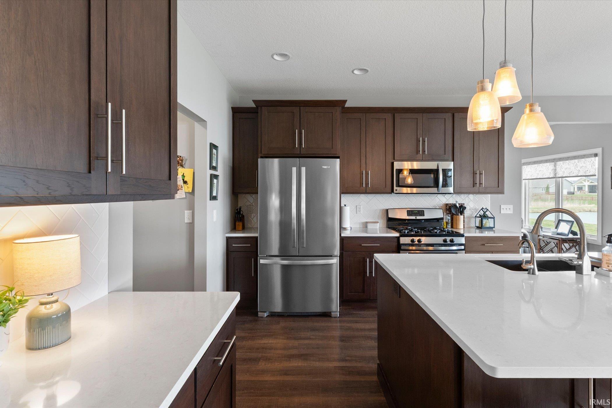 Kitchen featuring stainless steel appliances, dark wood finish cabinets, pendant lighting, dark wood-style floors, and tasteful backsplash