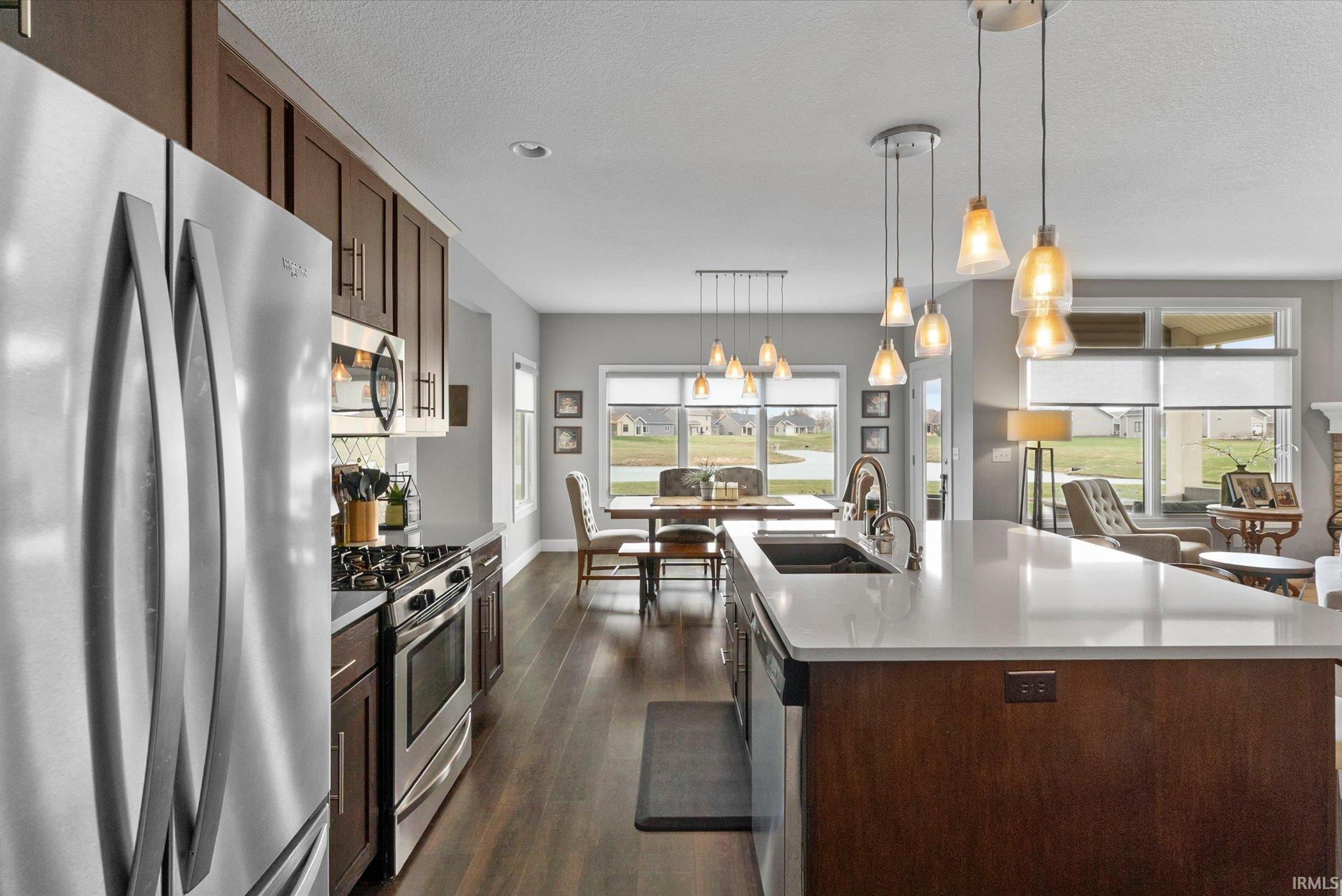 Kitchen with stainless steel appliances, dark wood finish cabinets, dark wood-type flooring, a center island with sink, and suspended lighting