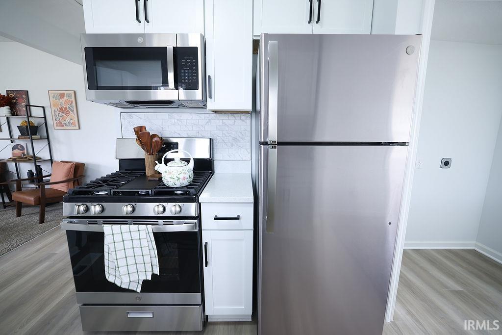 Kitchen featuring stainless steel appliances, white cabinets, light wood-style flooring, and tasteful backsplash