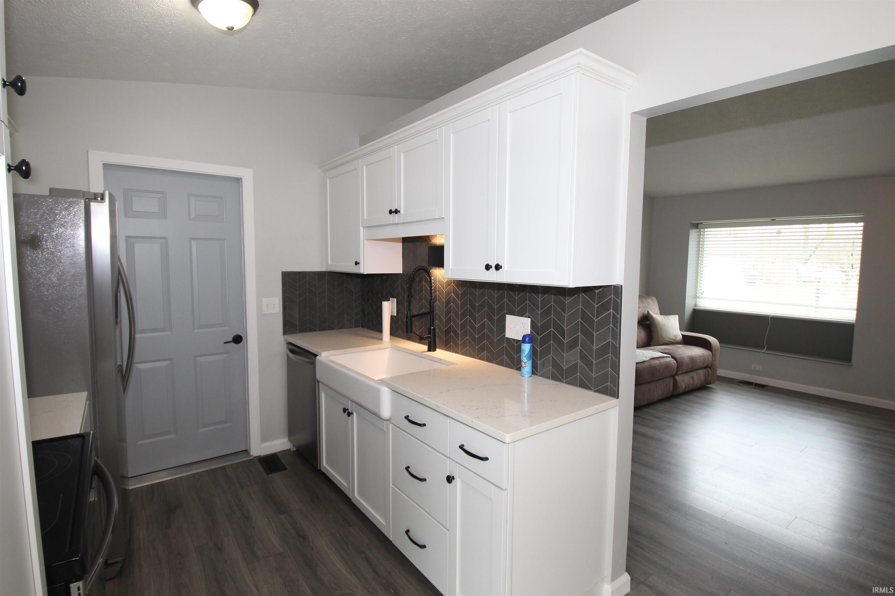 Kitchen featuring decorative backsplash, white cabinets, stainless steel appliances, dark wood-style flooring, and a textured ceiling