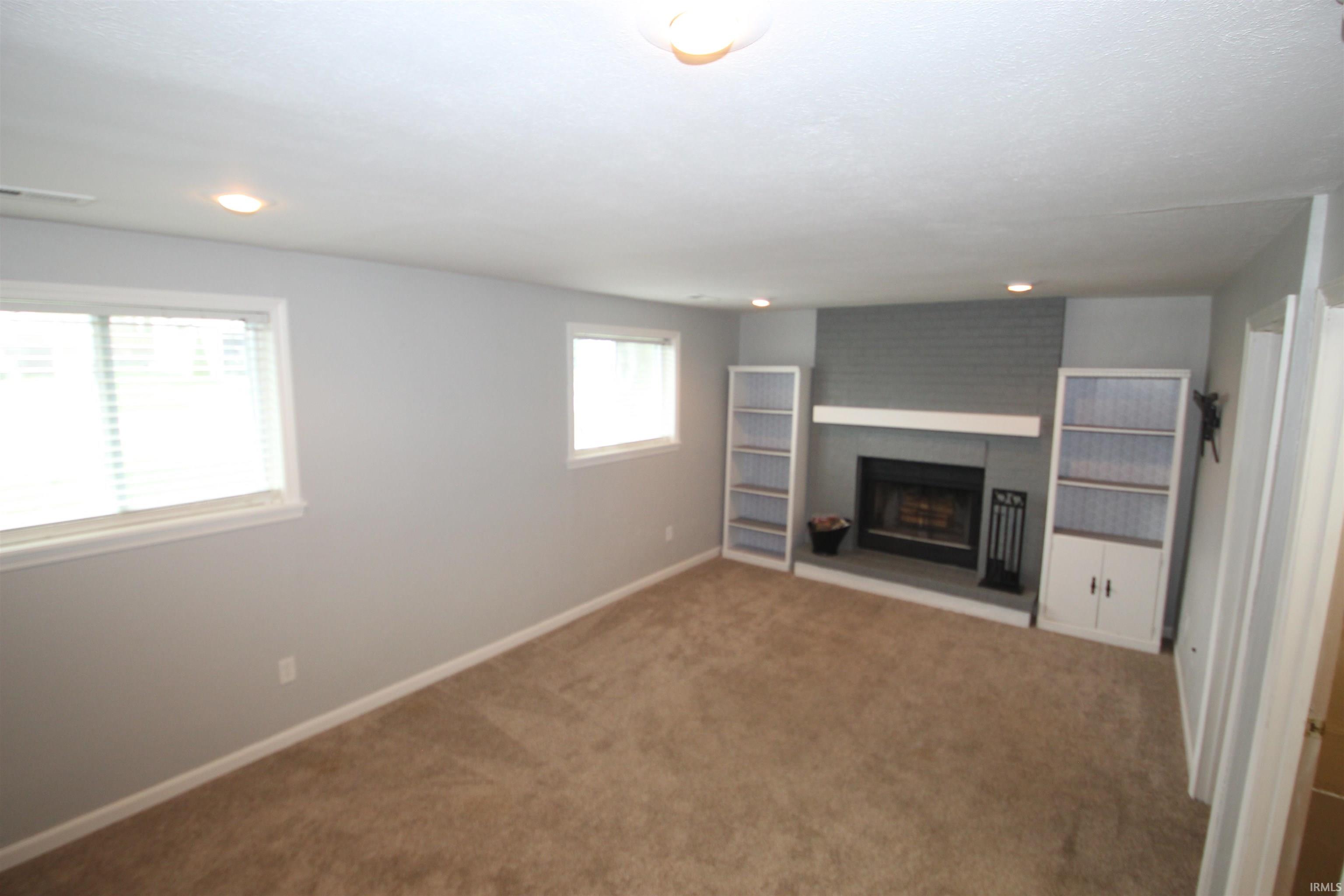 Unfurnished living room with carpet floors, a brick fireplace, and recessed lighting