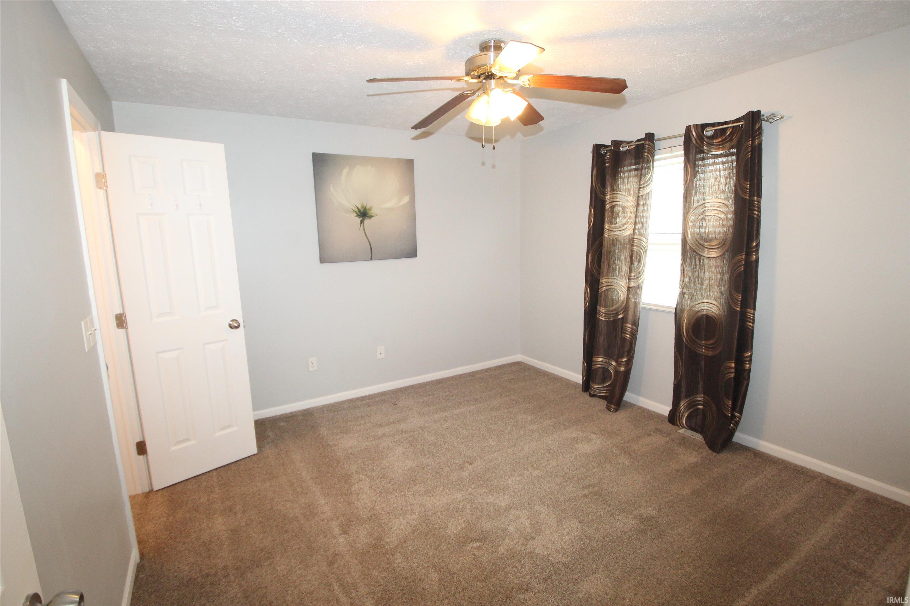 Unfurnished room featuring a textured ceiling, dark carpet, and ceiling fan