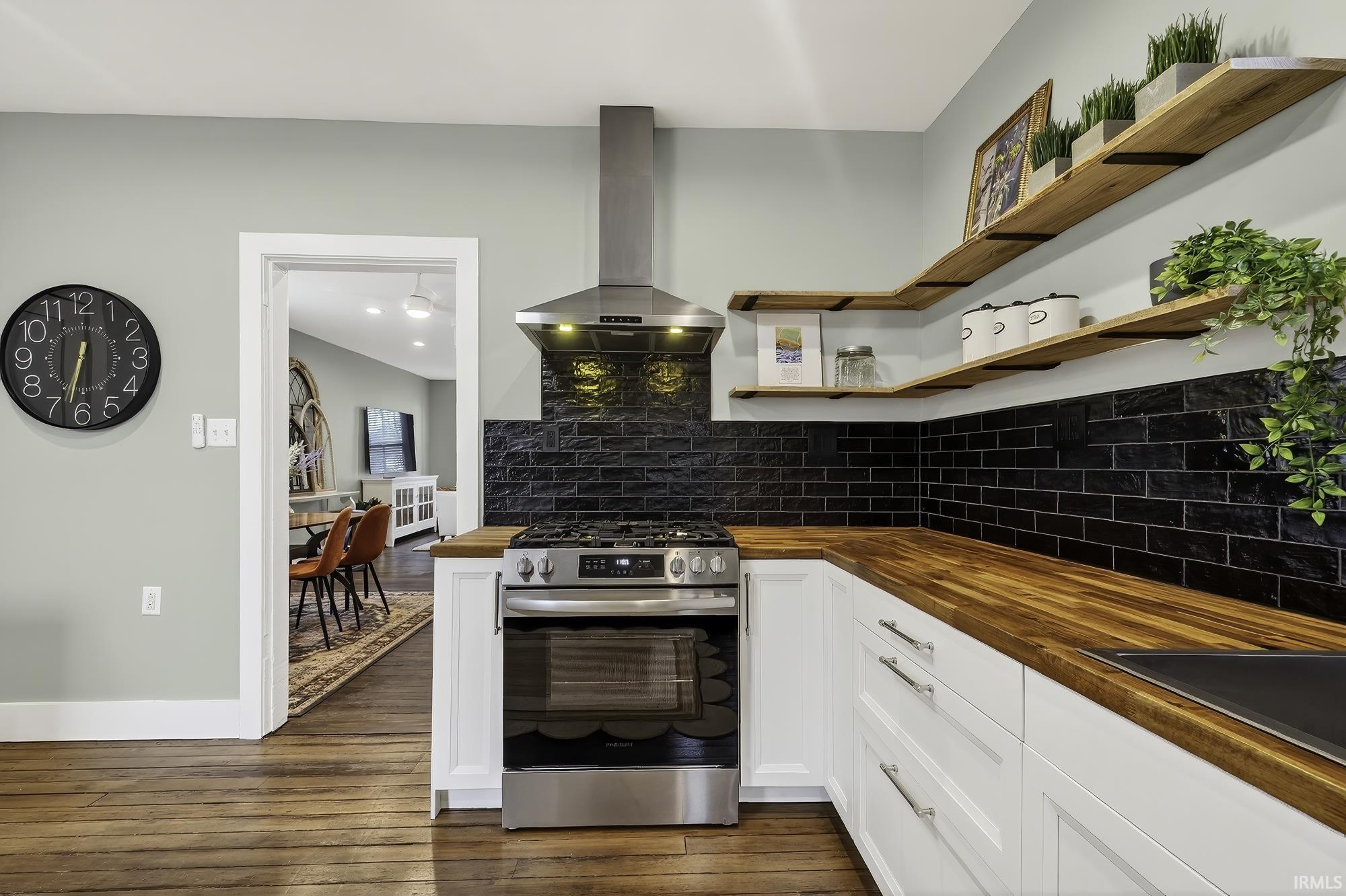 Kitchen with wooden counters, open shelves, gas stove, extractor fan, and white cabinets