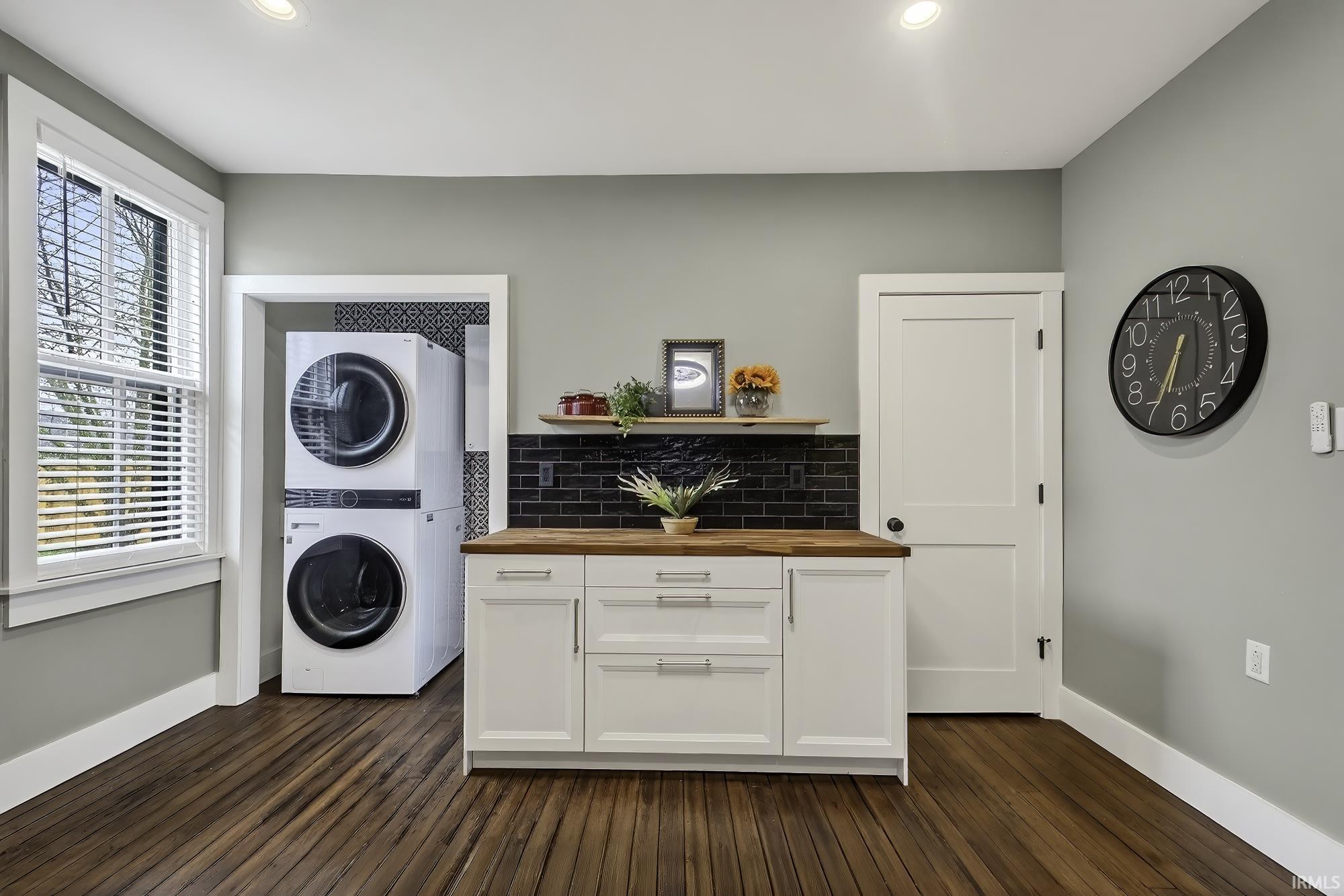 Laundry room with stacked washer and dryer, dark wood-type flooring, and recessed lighting