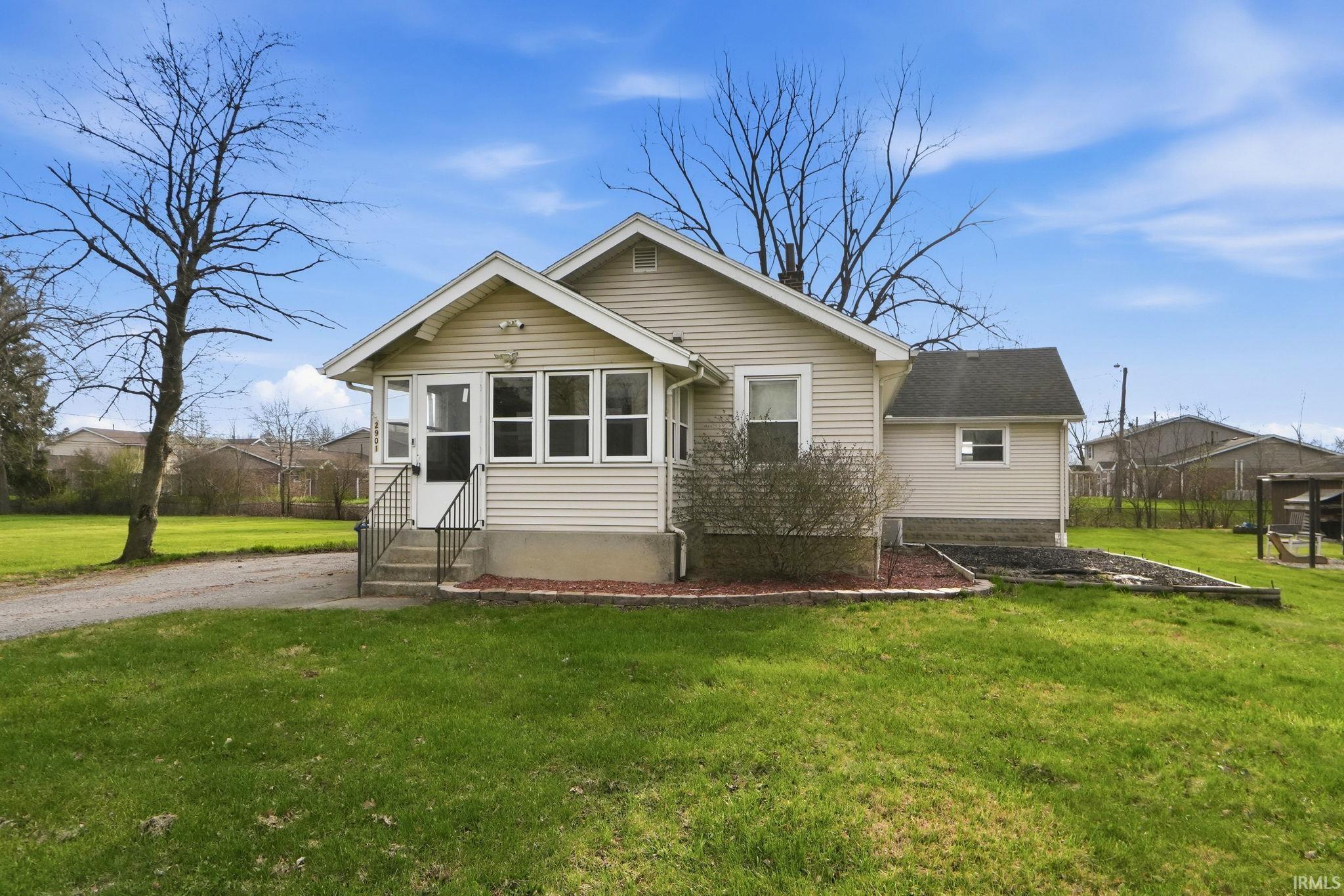Rear view of property featuring a lawn, a sunroom, and entry steps