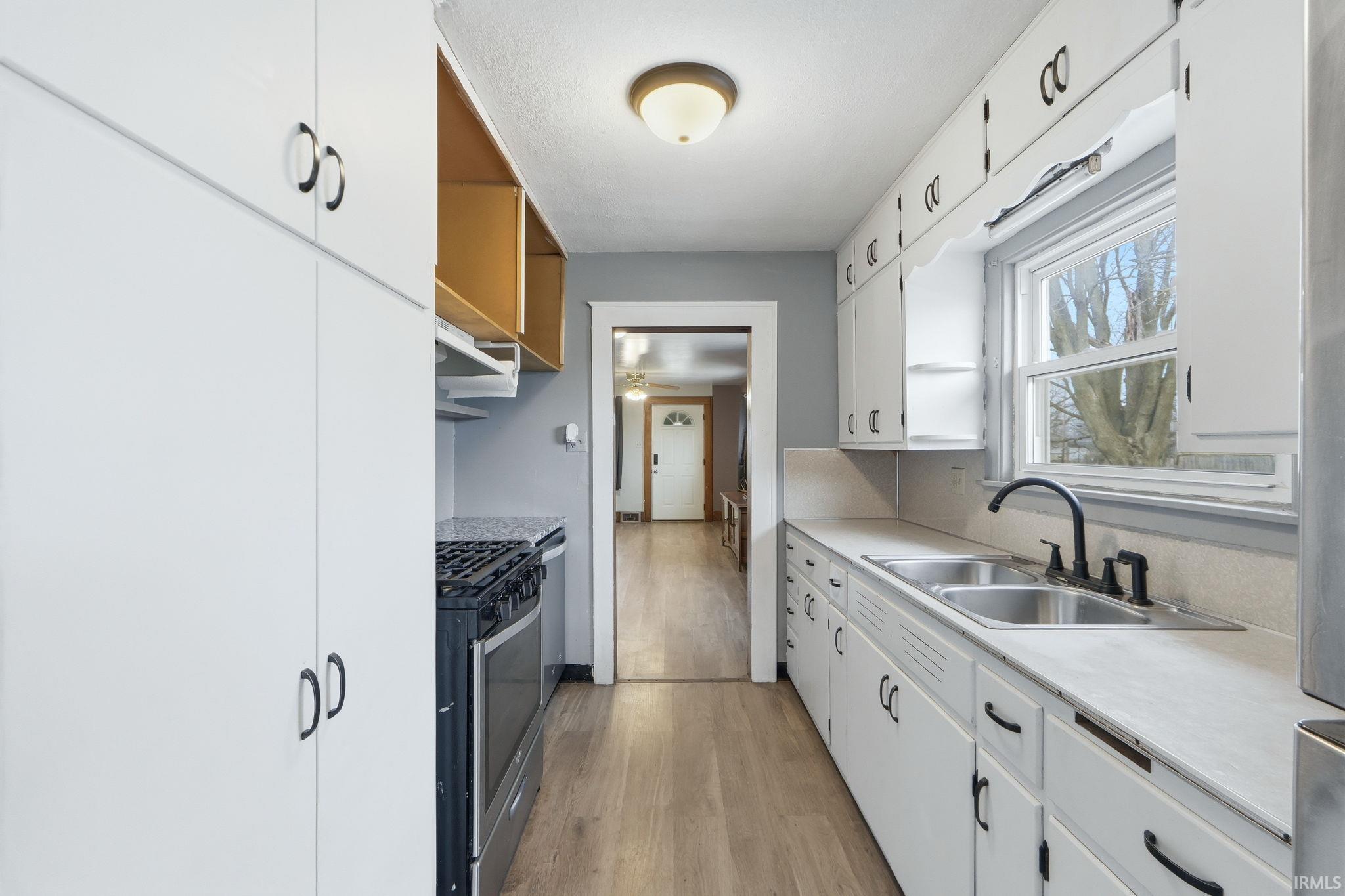 Kitchen with white cabinets, stainless steel appliances, light countertops, and light wood-style floors
