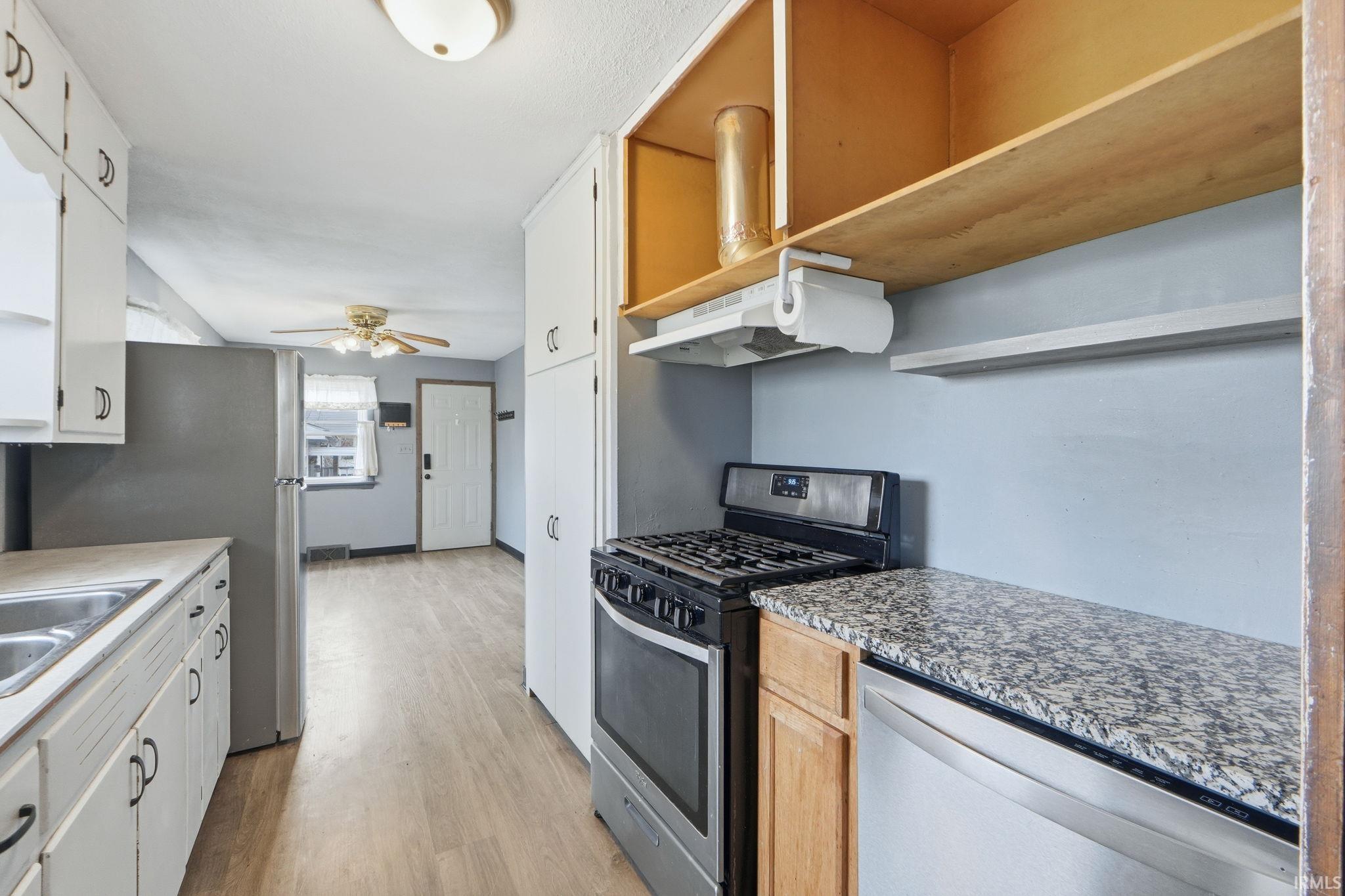 Kitchen featuring stainless steel appliances, light wood-type flooring, open shelves, light countertops, and a ceiling fan