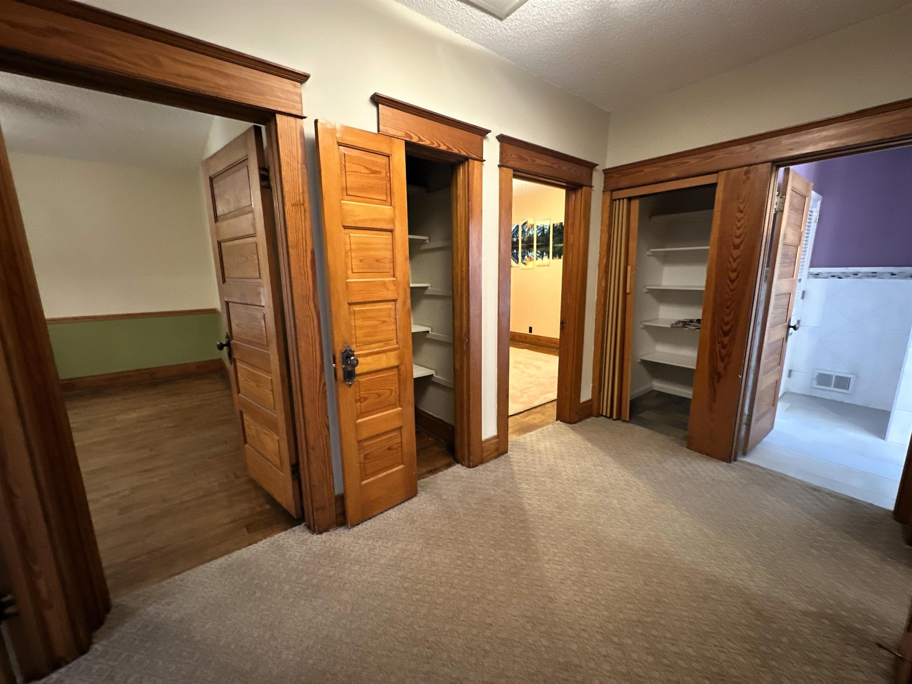 Unfurnished bedroom with a textured ceiling, light carpet, and multiple closets