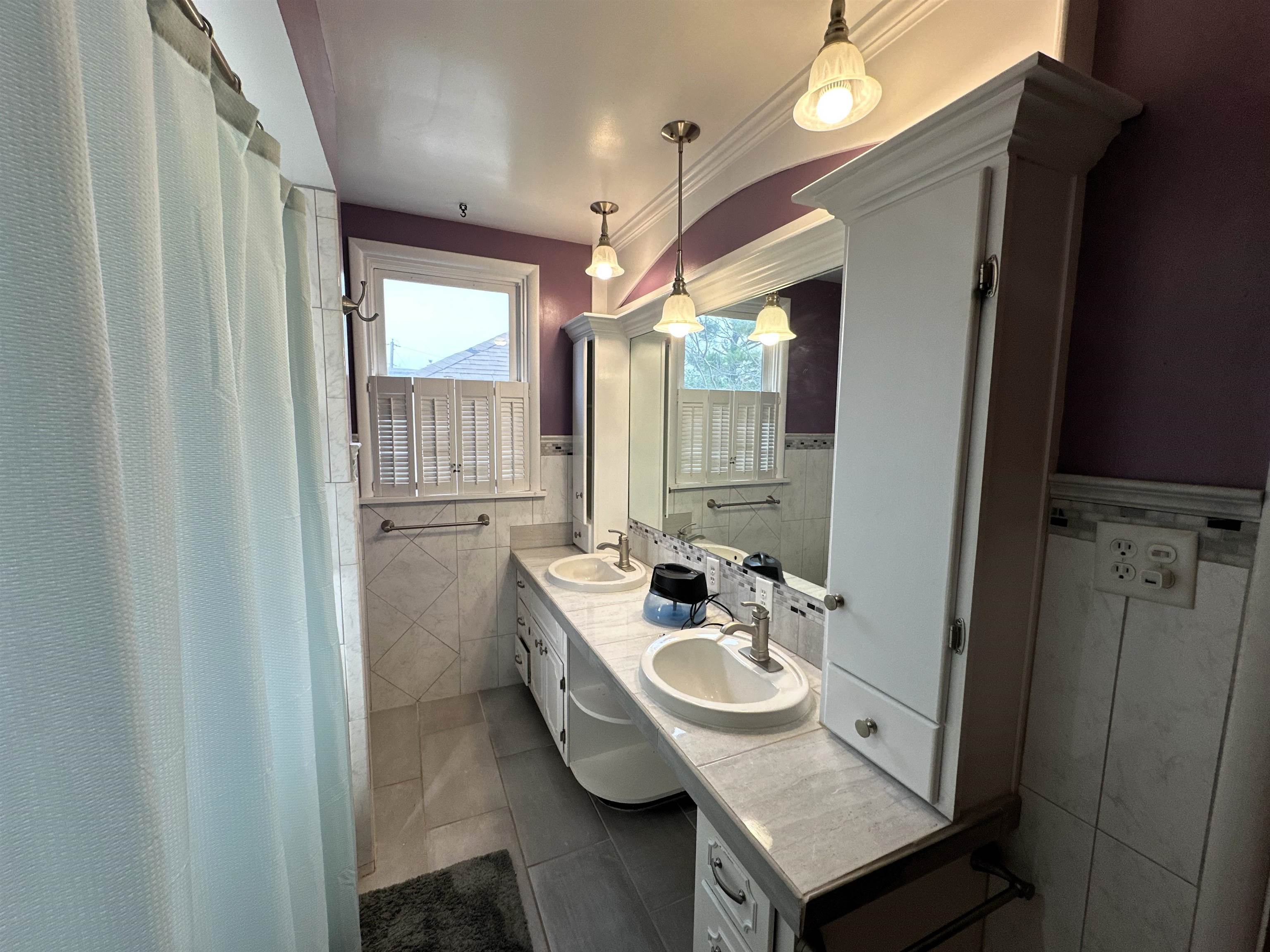 Bathroom with double vanity, dark tile patterned floors, a wainscoted wall, tile walls, and curtained shower