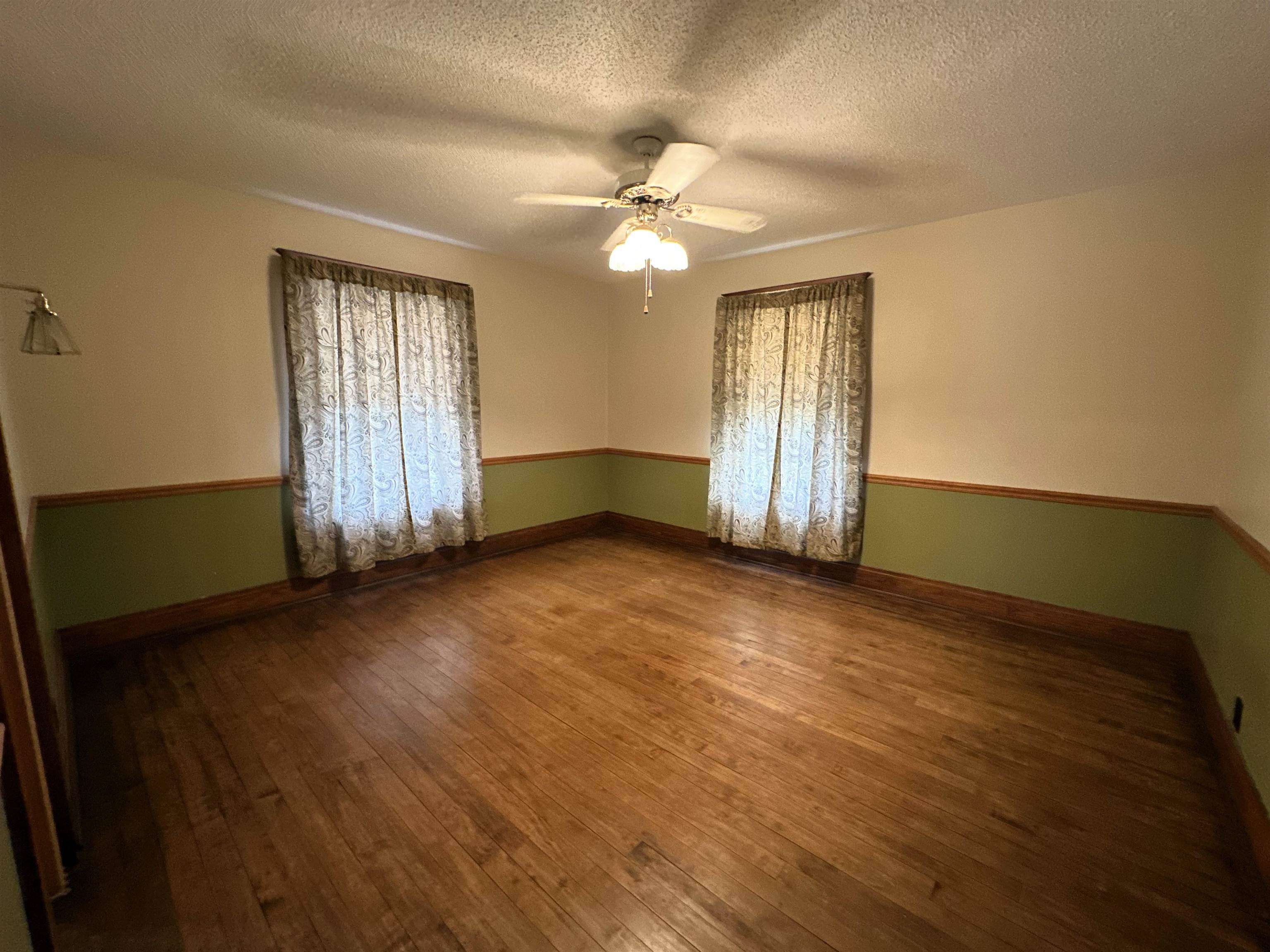 Empty room with hardwood / wood-style floors, ceiling fan, and a textured ceiling