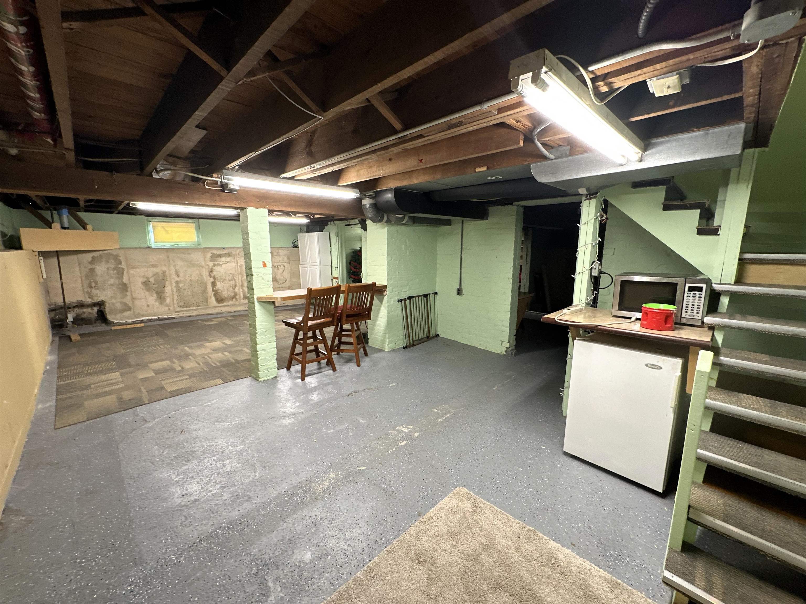 Unfinished below grade area featuring stairway and freestanding refrigerator
