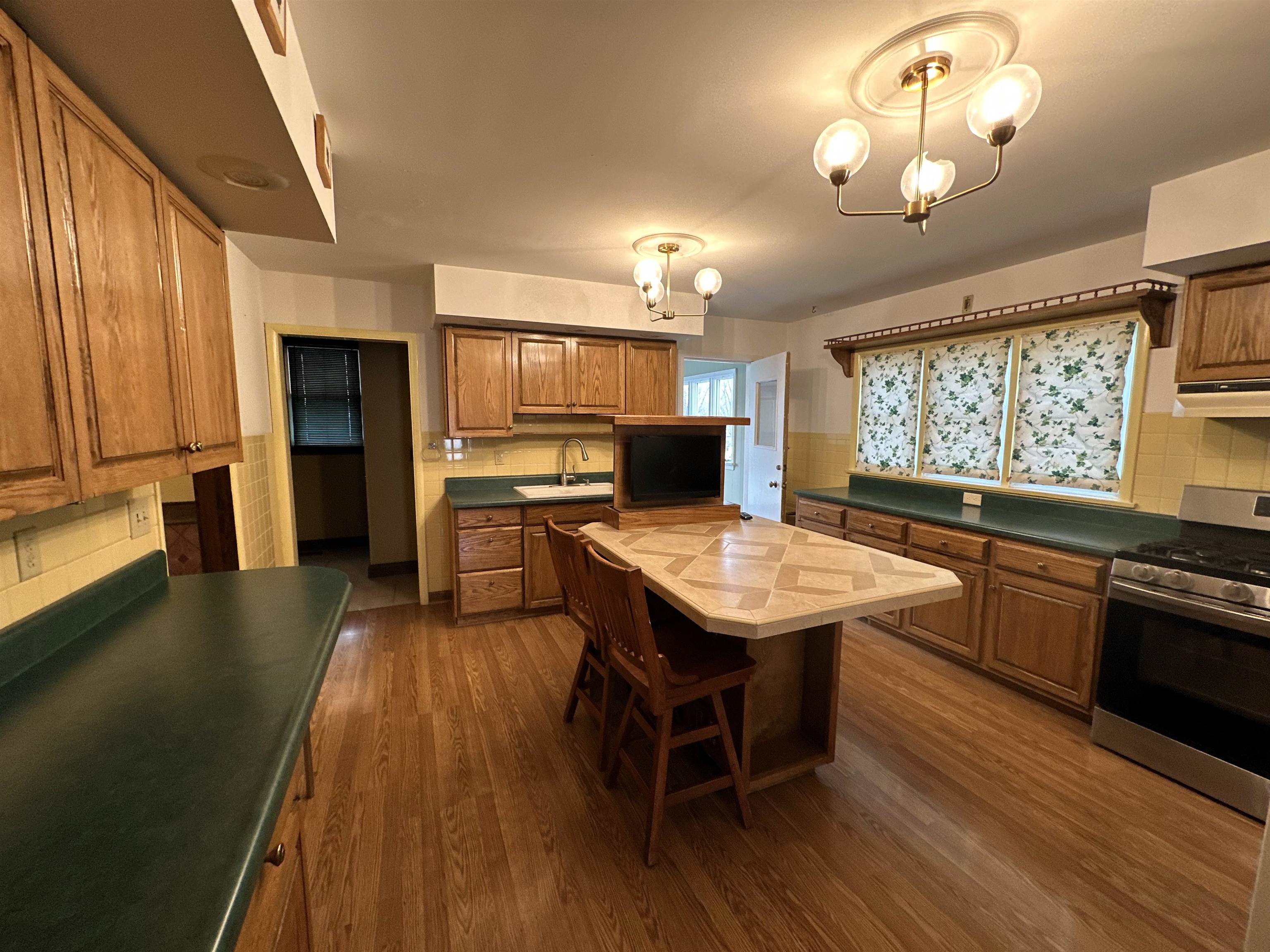 Kitchen with gas stove, wood finish cabinets, dark countertops, dark wood-style floors, and decorative backsplash