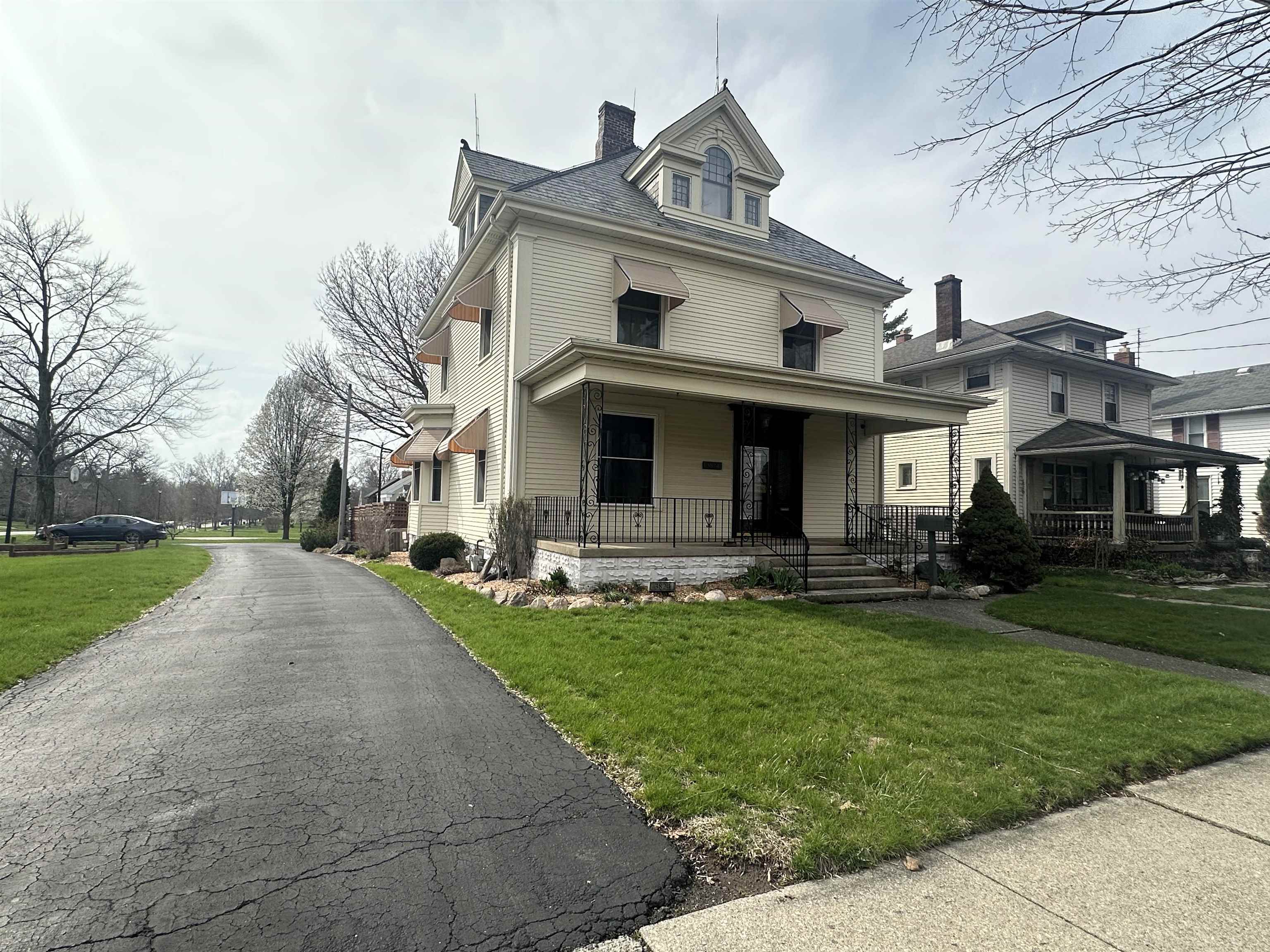 Traditional style home featuring a front lawn, a chimney, a porch, and roof with shingles