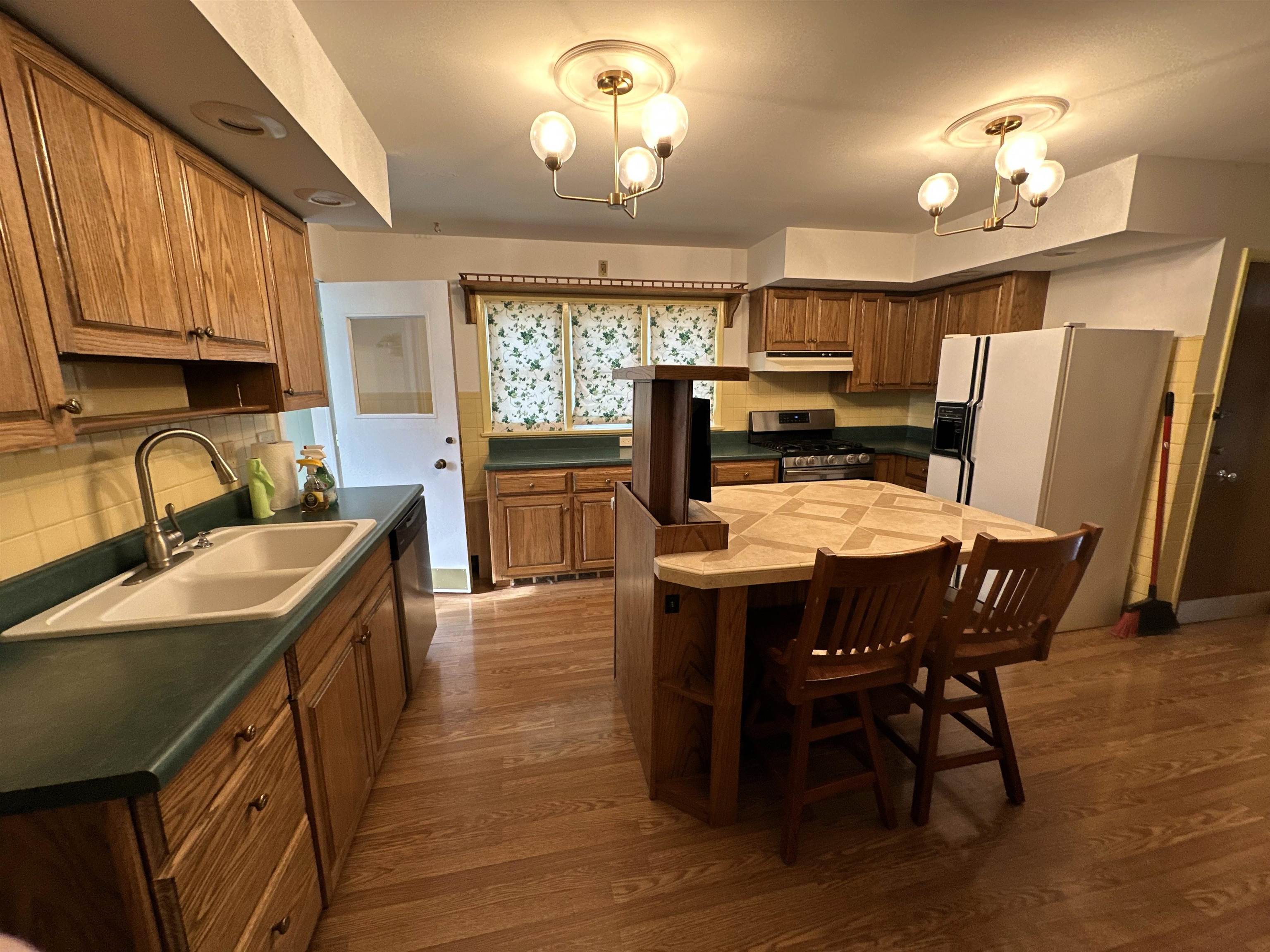 Kitchen with wood finish cabinetry, white refrigerator with ice dispenser, a breakfast bar, gas range, and a center island
