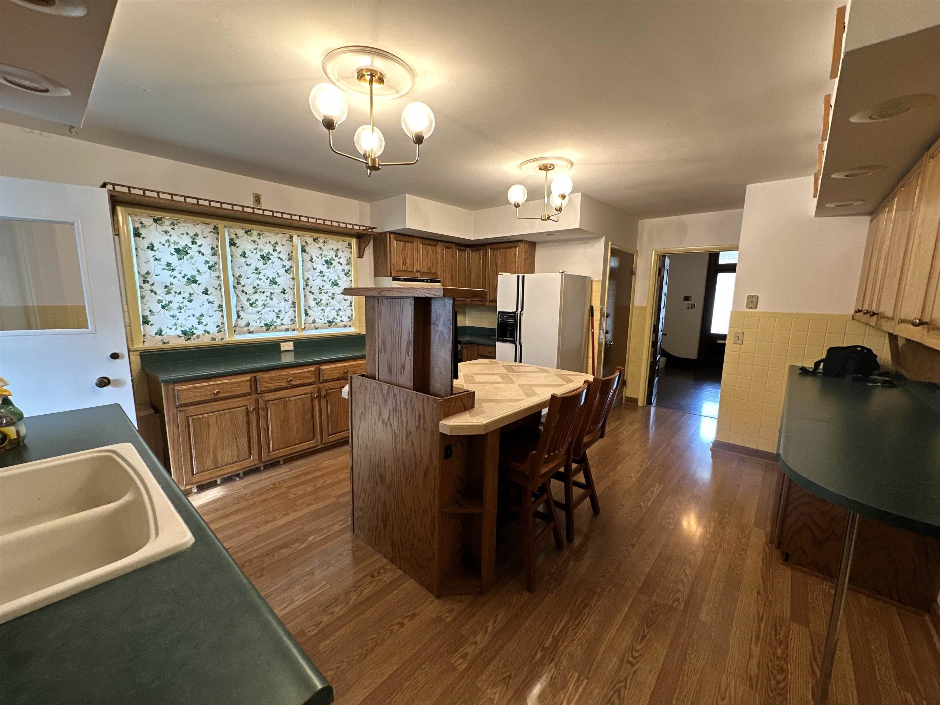 Kitchen featuring dark countertops, wood finish cabinets, white fridge with ice dispenser, dark wood-style floors, and wainscoting