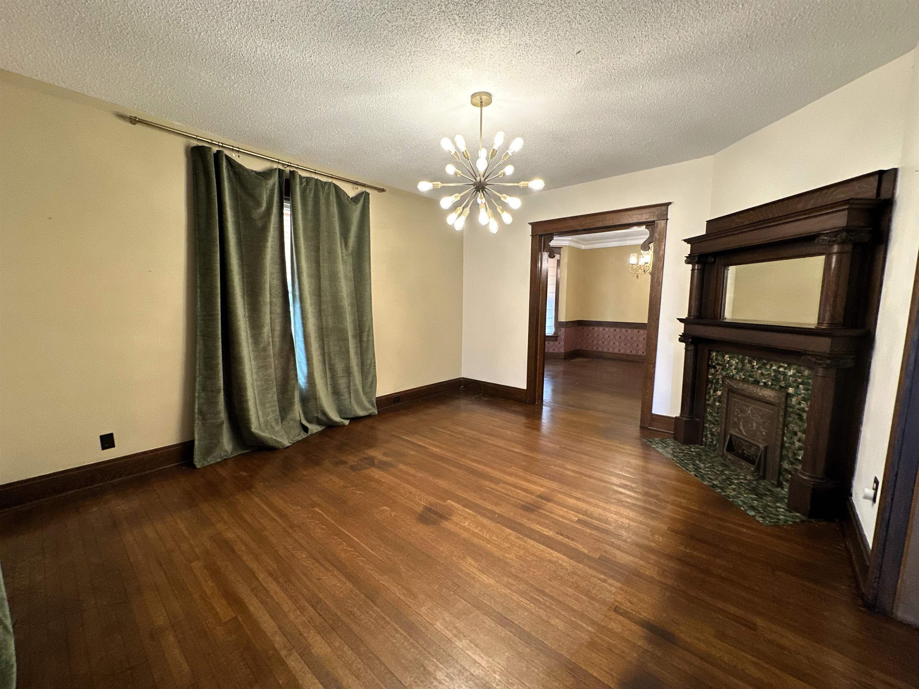 Unfurnished living room with dark wood-style flooring, hanging lights, a textured ceiling, and a tile fireplace