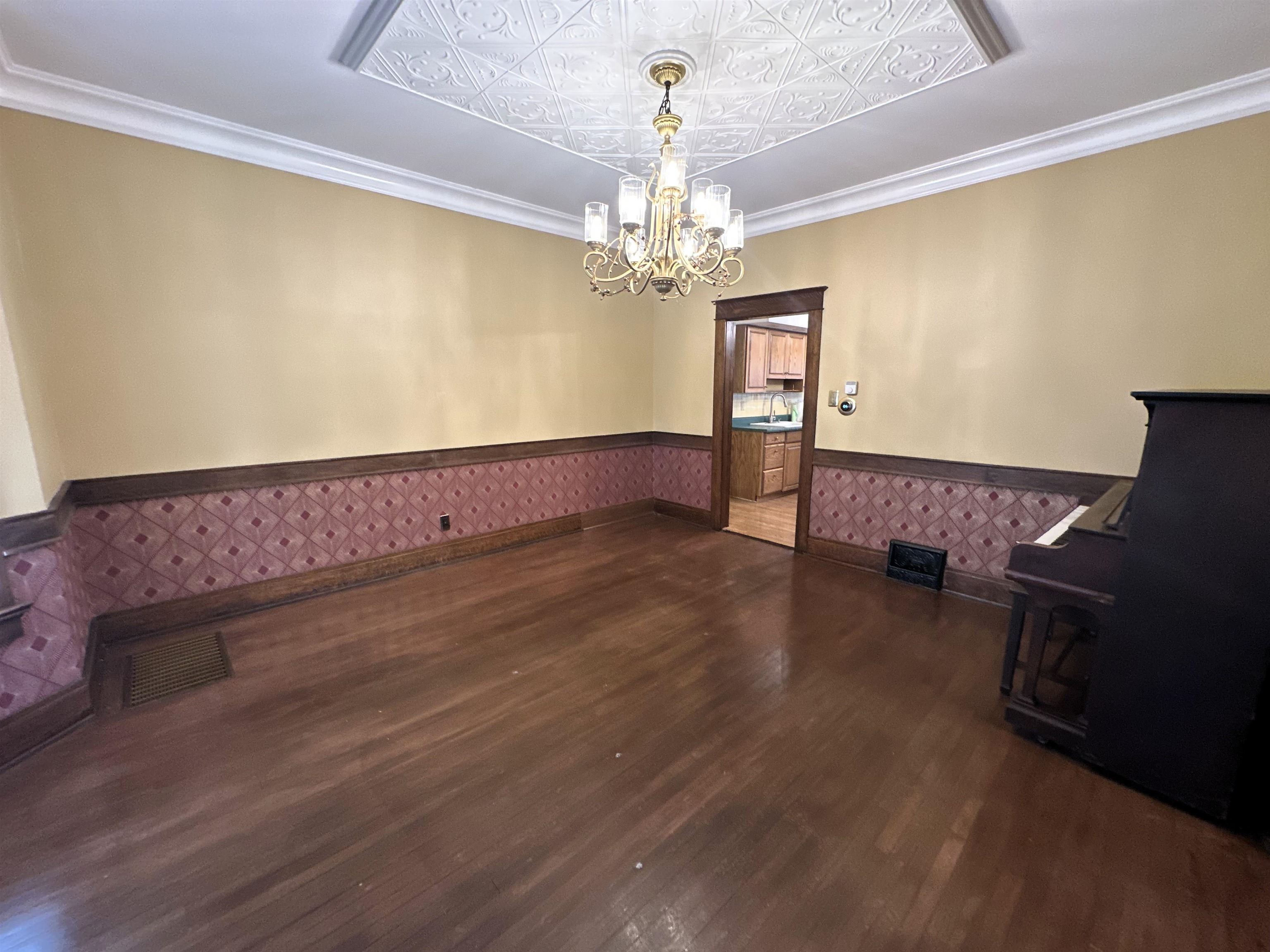 Unfurnished dining area with dark wood-style flooring, a wainscoted wall, a chandelier, and ornamental molding