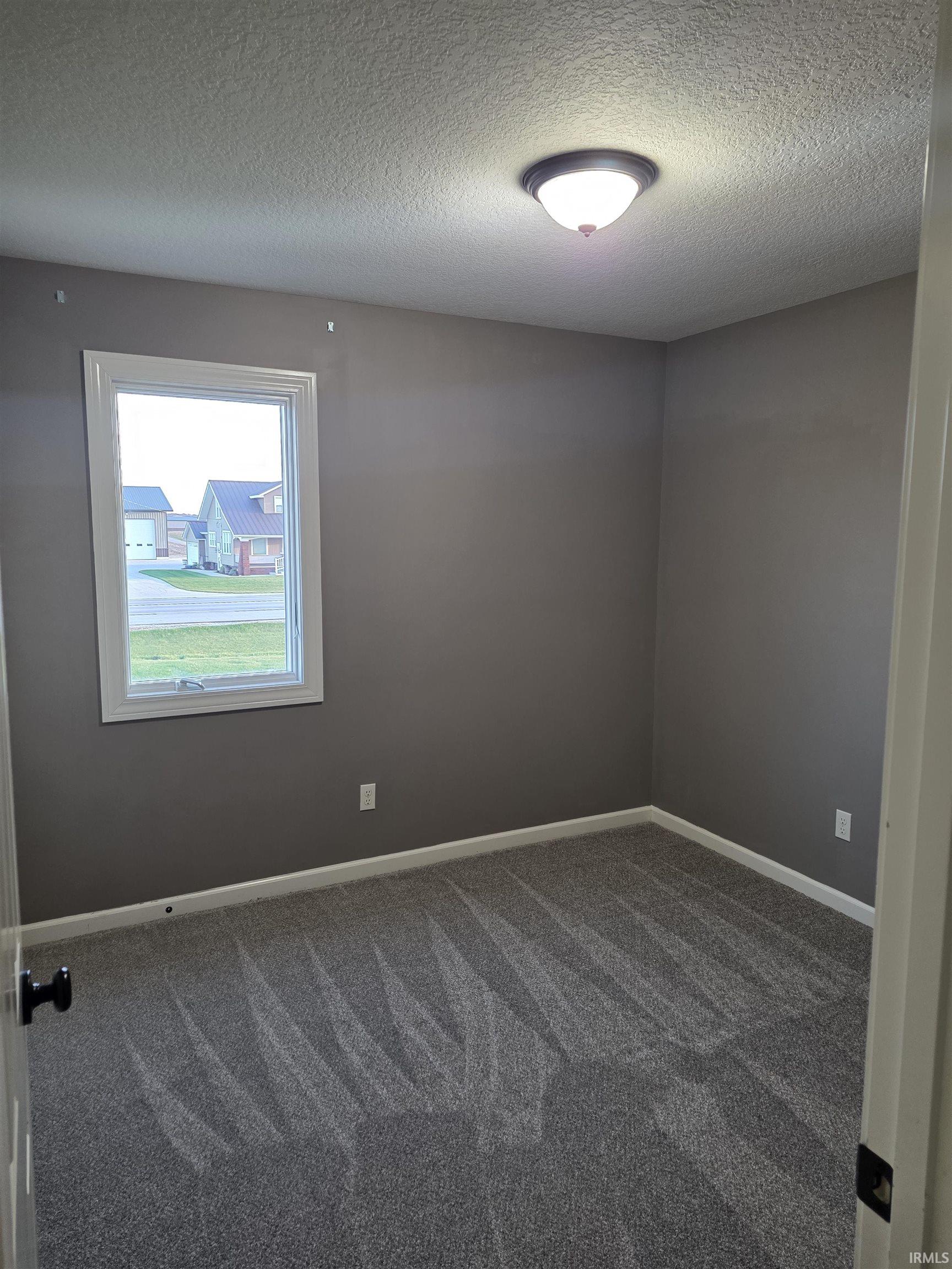 Spare room with a textured ceiling and dark colored carpet