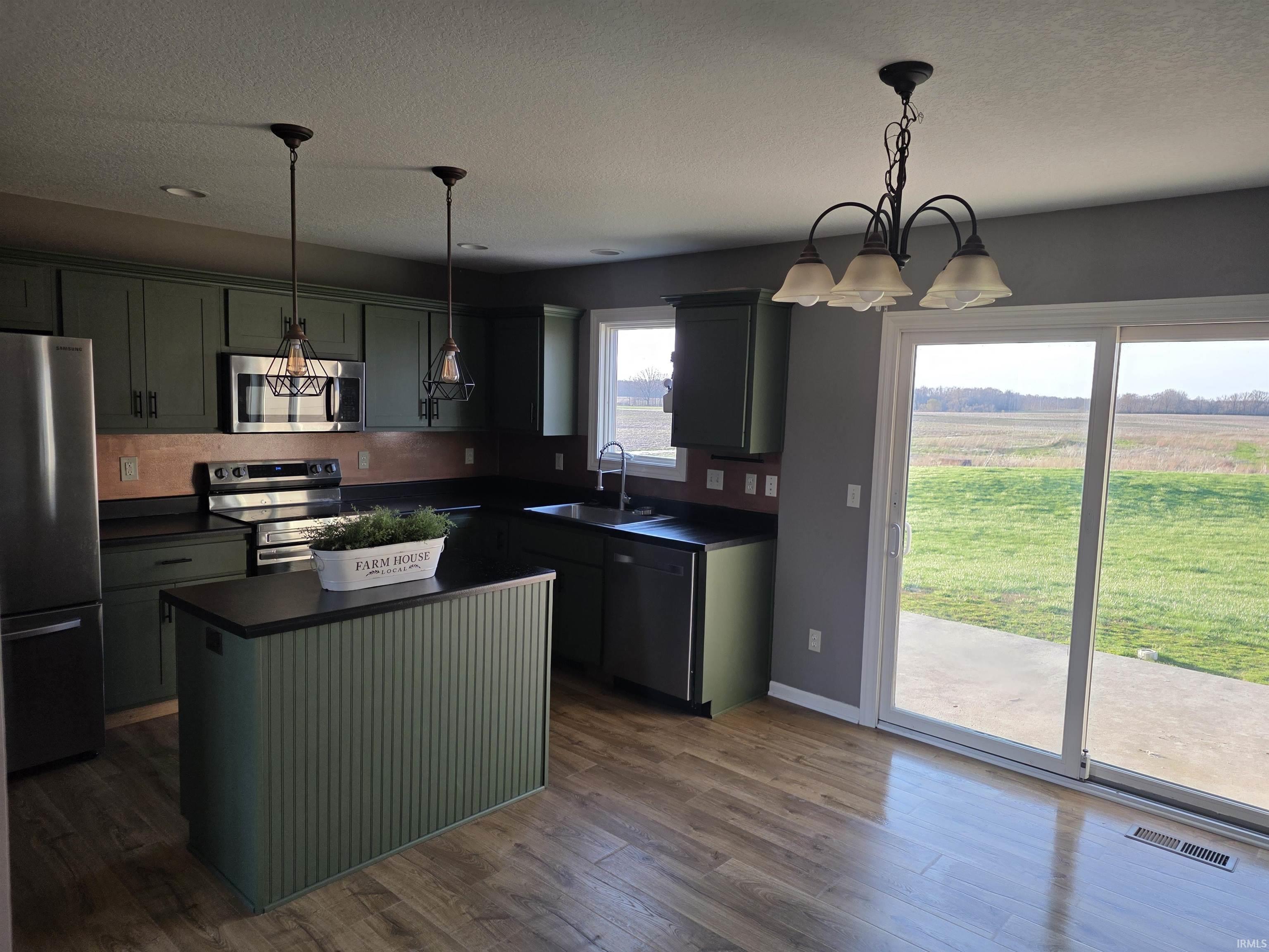 Kitchen with green cabinets, dark countertops, a kitchen island, stainless steel appliances, and a textured ceiling