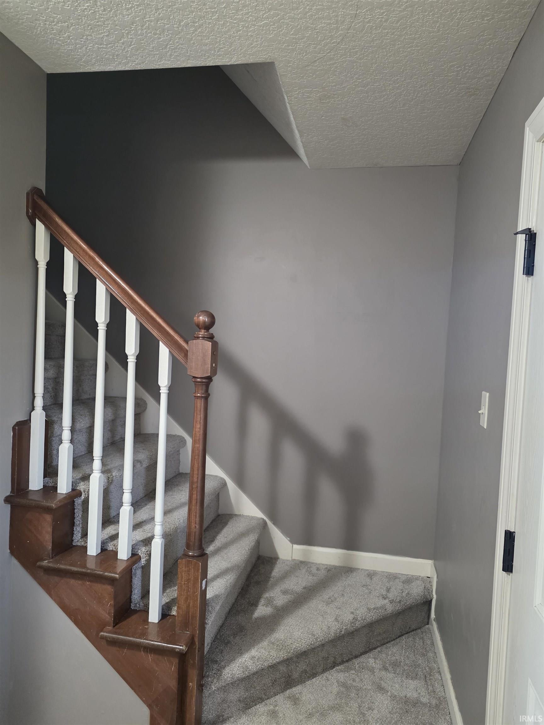 Staircase featuring a textured ceiling and carpet flooring