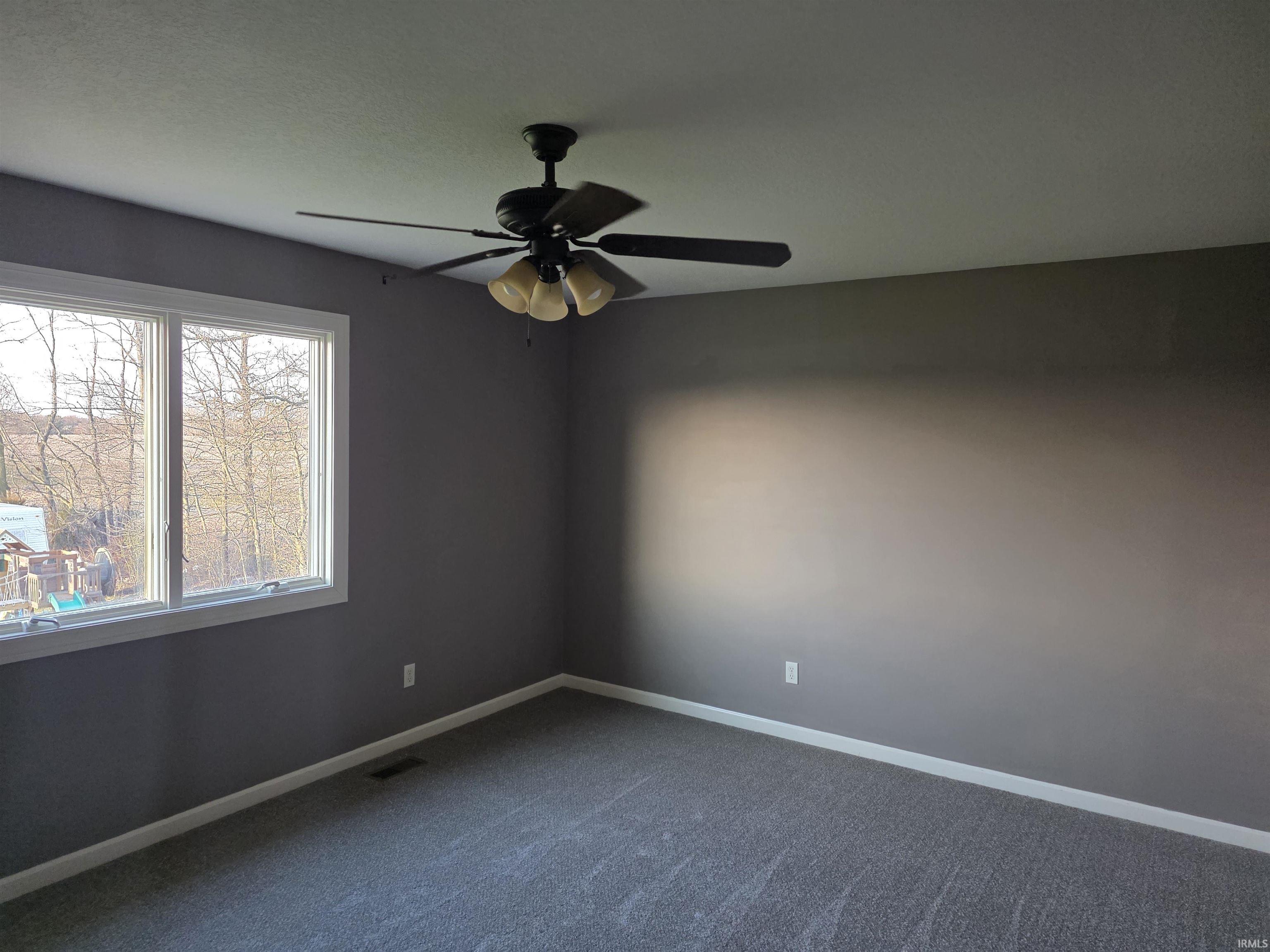 Empty room with a ceiling fan and dark colored carpet
