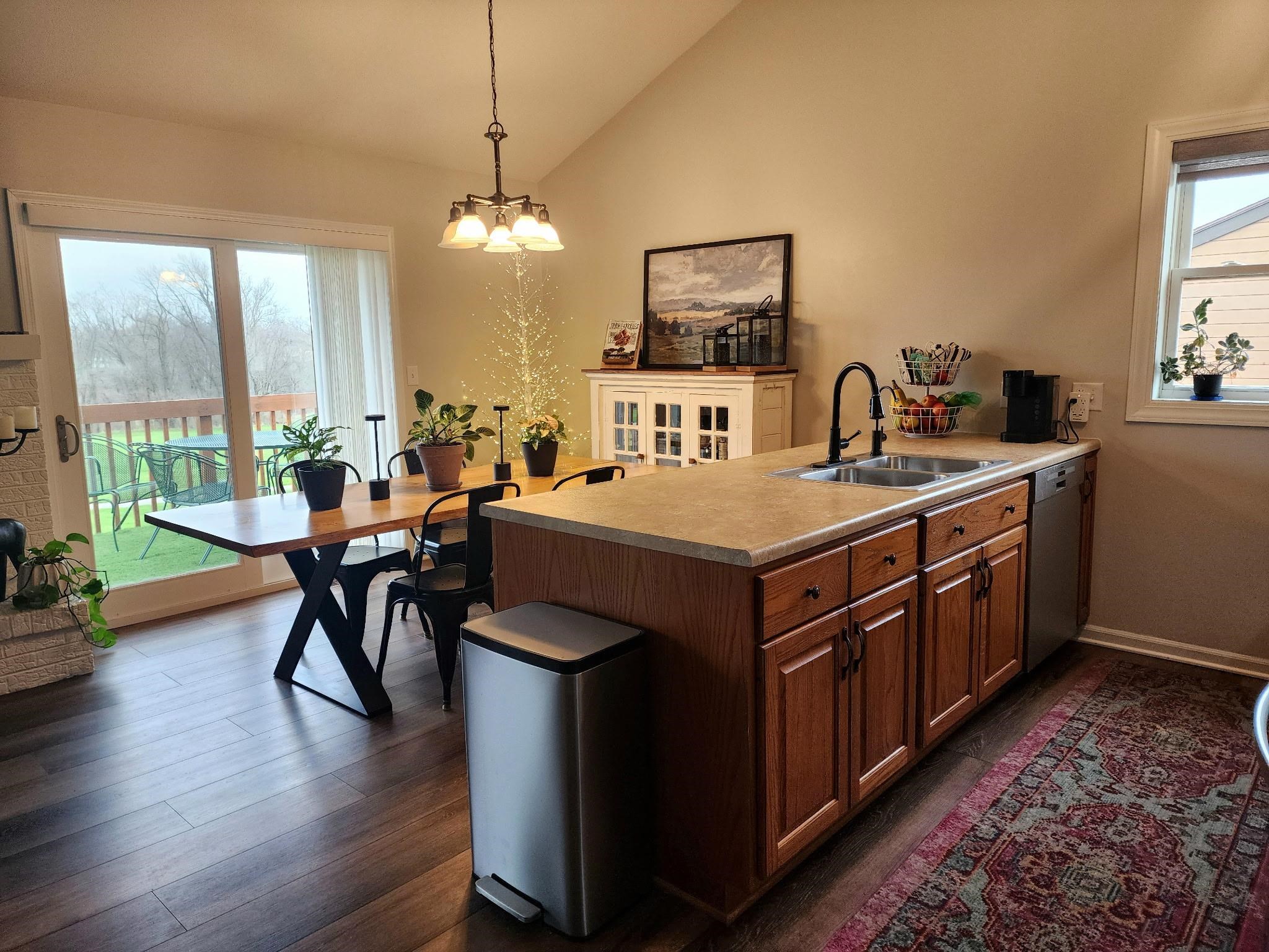 Kitchen featuring a peninsula, vaulted ceiling, wood finish cabinetry, light countertops, and dishwasher