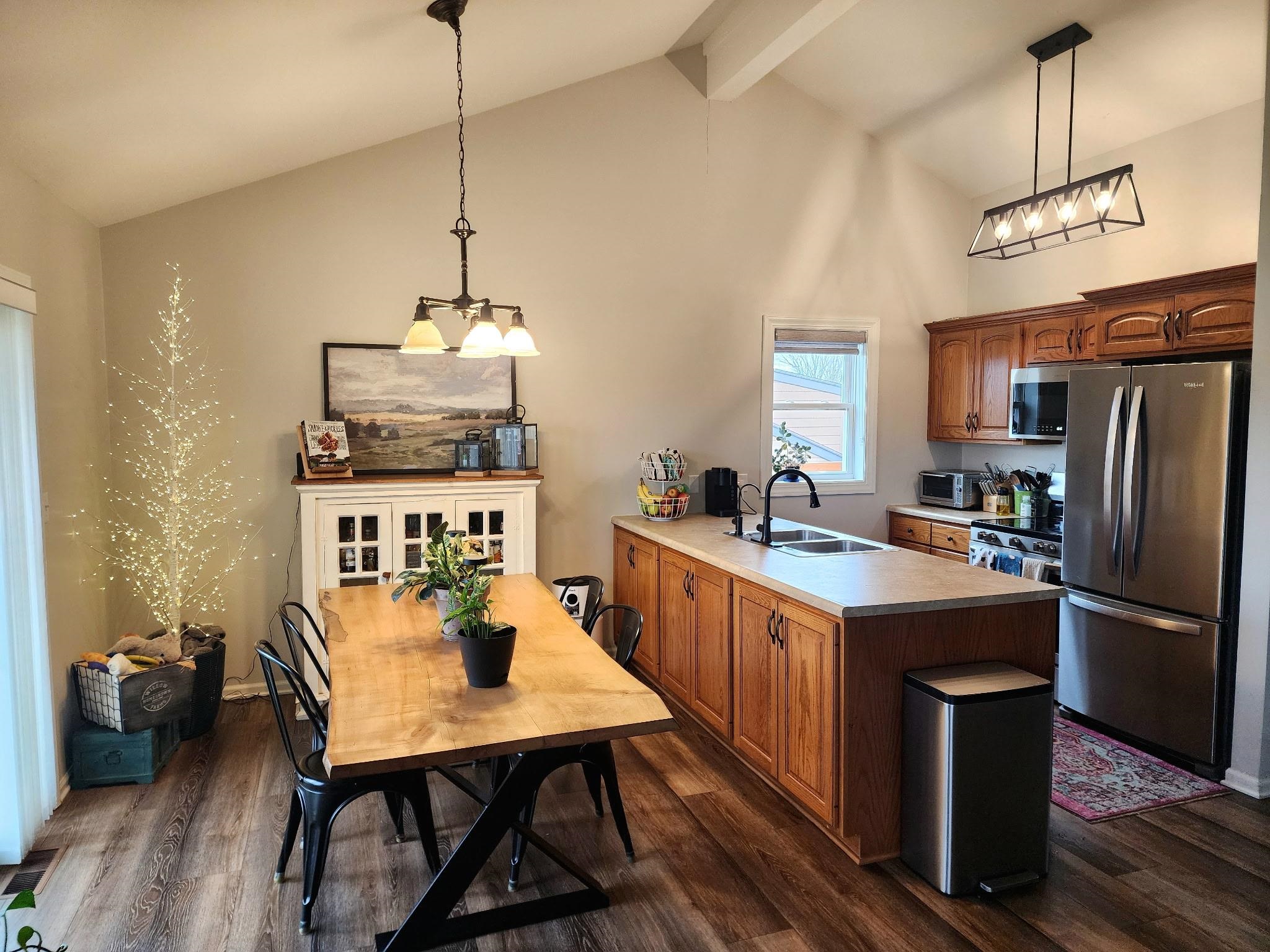 Kitchen featuring freestanding refrigerator, light countertops, a peninsula, wood finish cabinetry, and suspended lighting